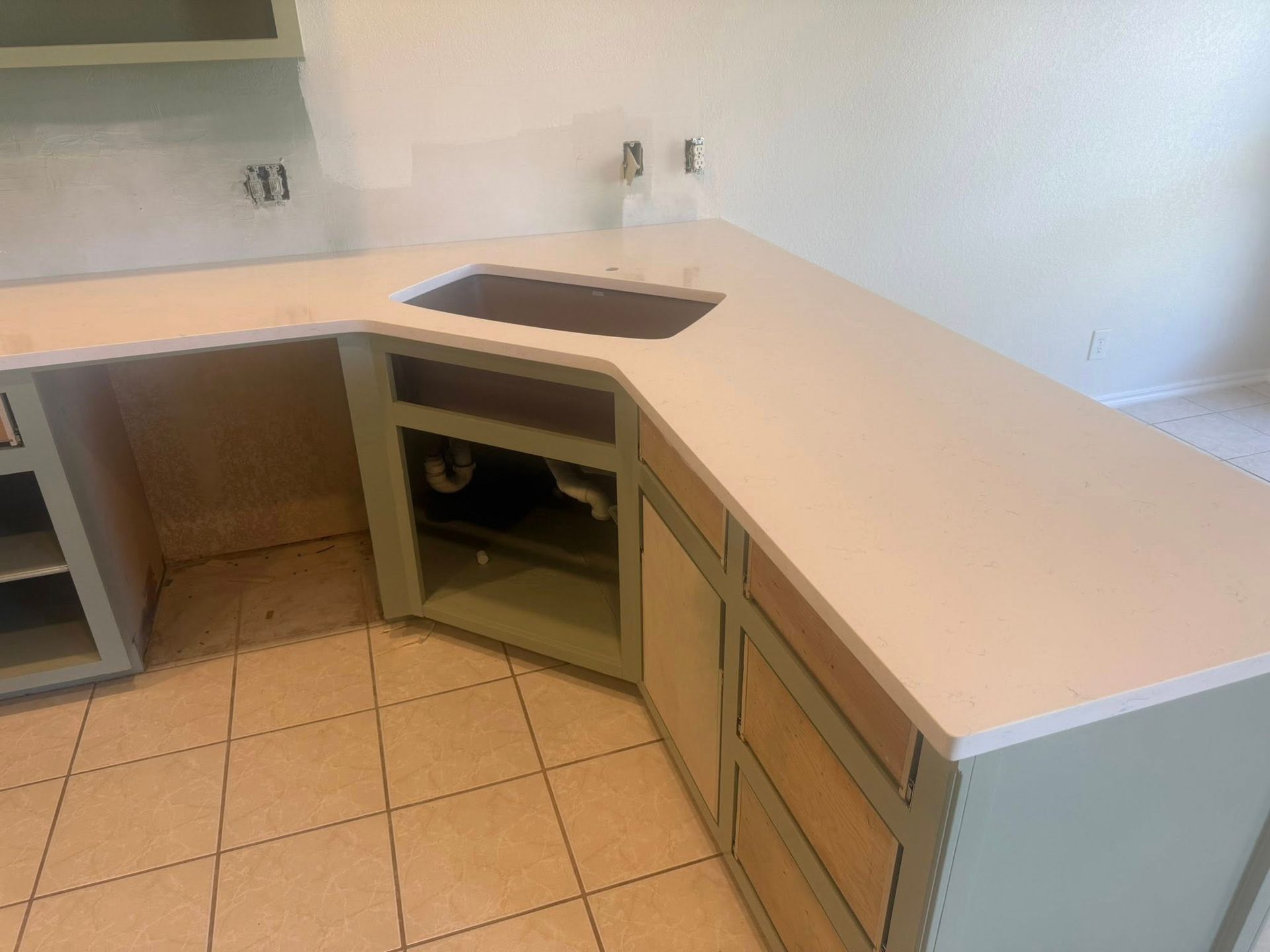 Empty kitchen with light wood cabinets, white countertops, and a built-in cooktop on a tiled floor