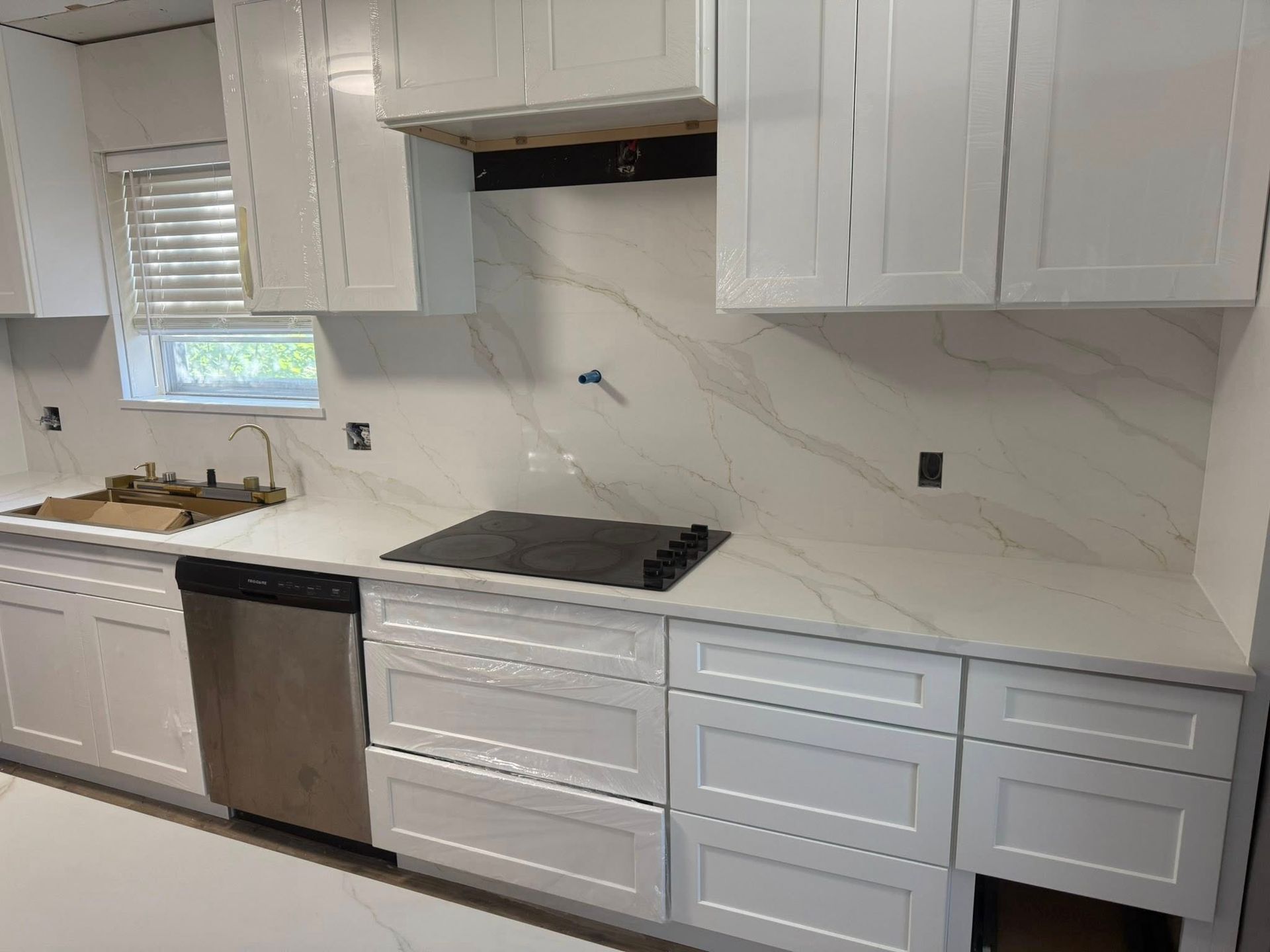 Modern white kitchen with gray cabinets, stainless dishwasher, black cooktop, and marble-look backsplash