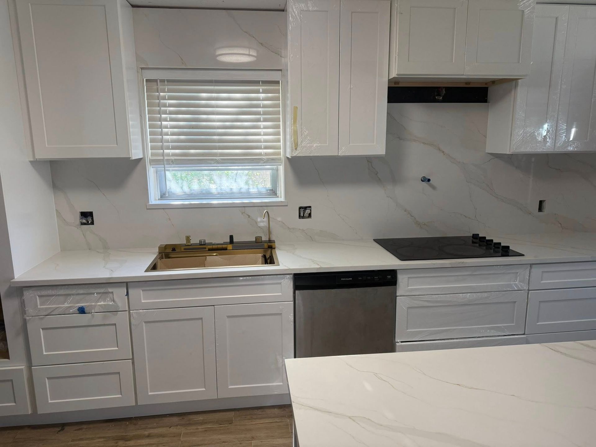 Modern white kitchen with cabinets, window, sink, dishwasher, cooktop, and island countertop