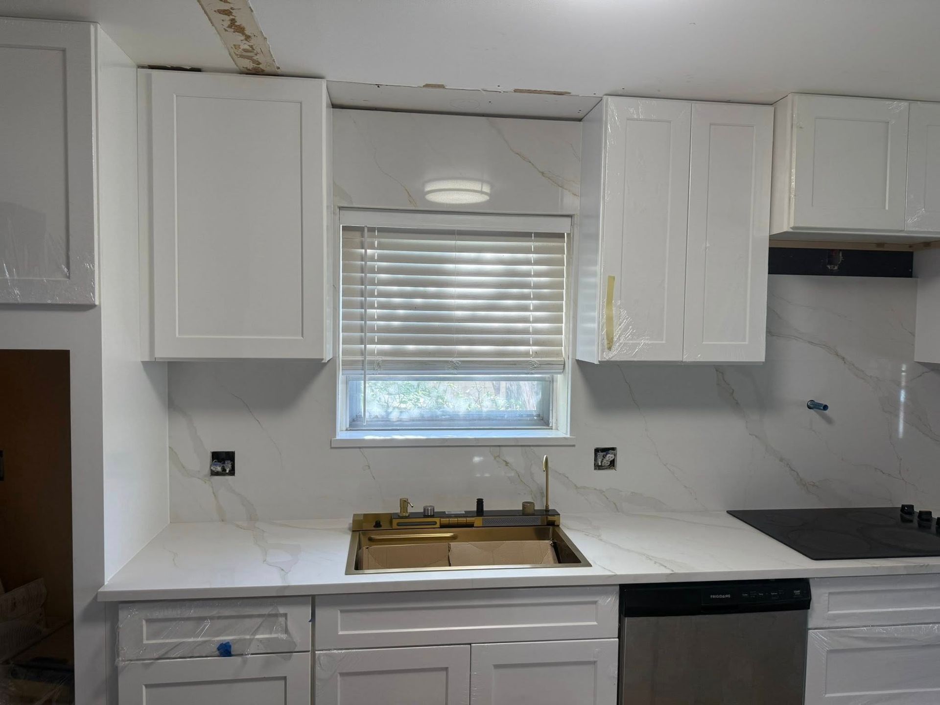 Small kitchen with white cabinets, marble-look countertops, window with blinds, and a gas cooktop.