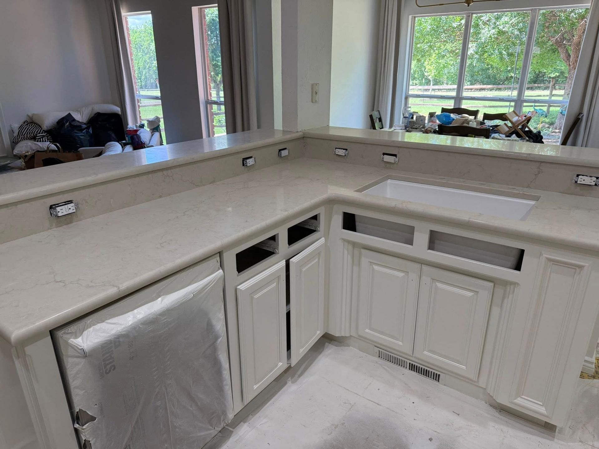 White kitchen corner with cabinets, countertop, and large windows overlooking a yard