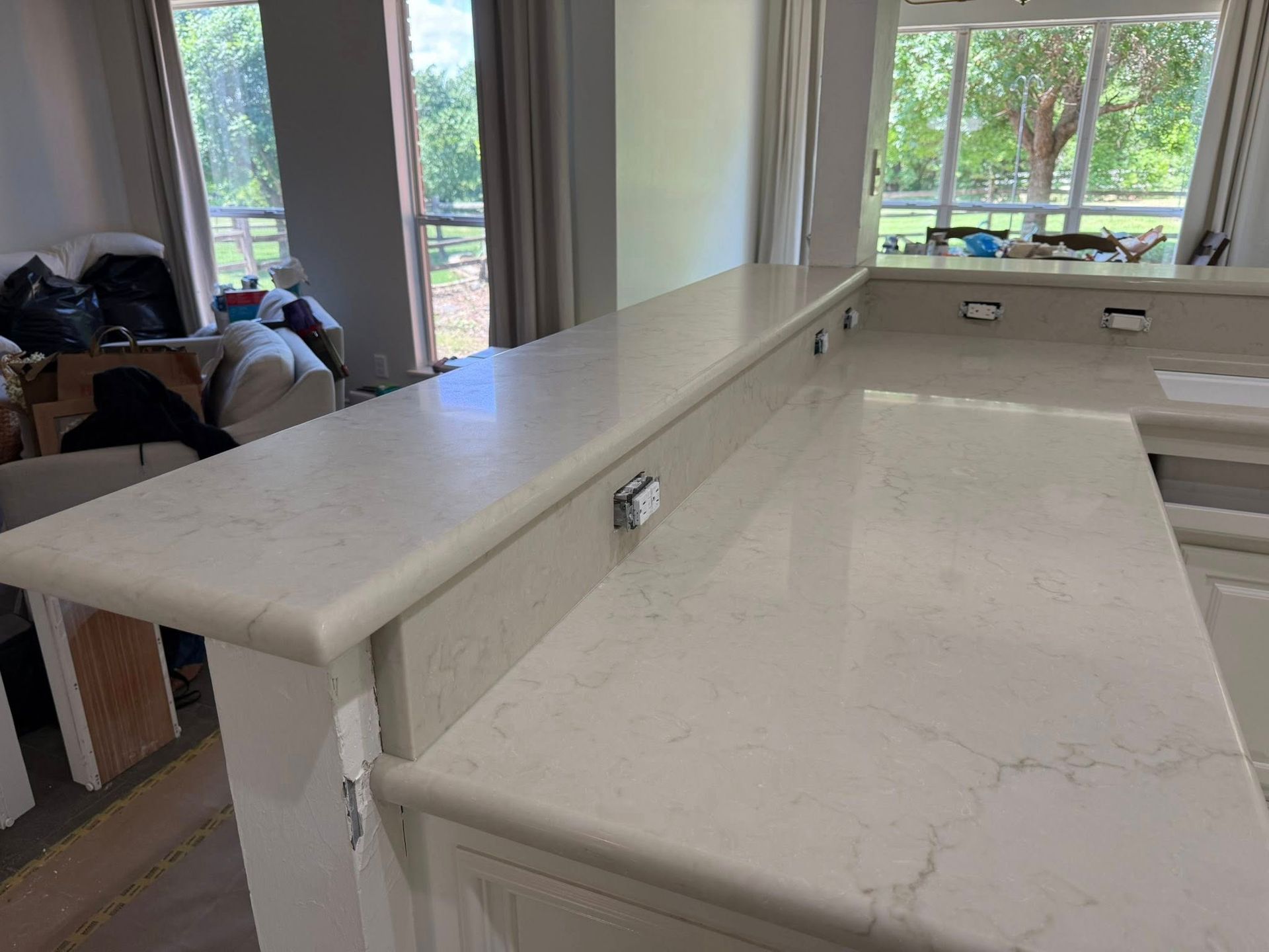 Kitchen counter with white marble island and bright windows overlooking trees