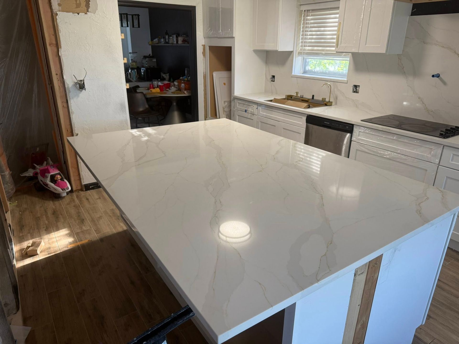 Bright modern kitchen with large white island countertop, white cabinets, and dark wood flooring
