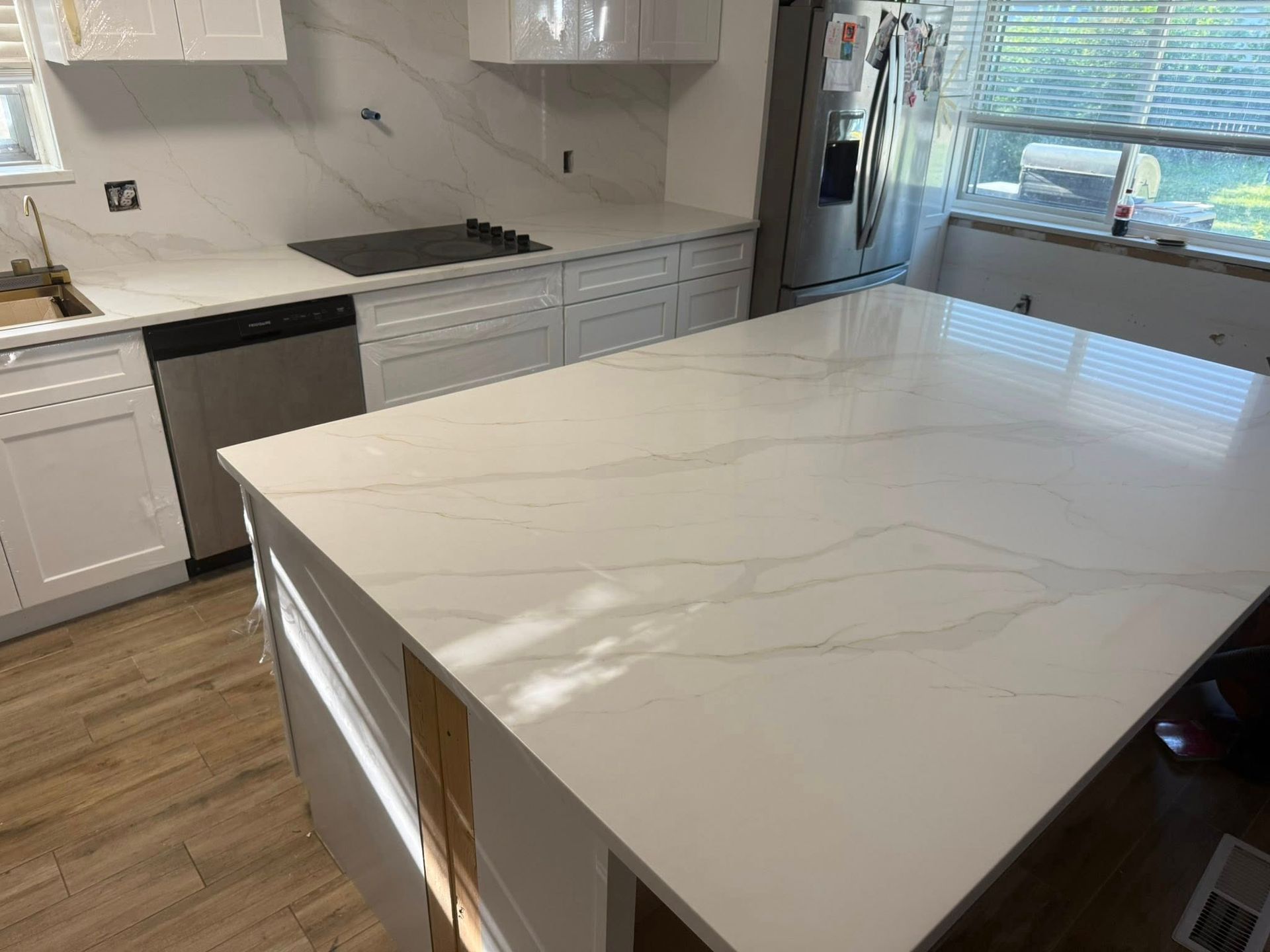 Modern white kitchen with marble island, white cabinets, wood floor, and stainless steel appliances