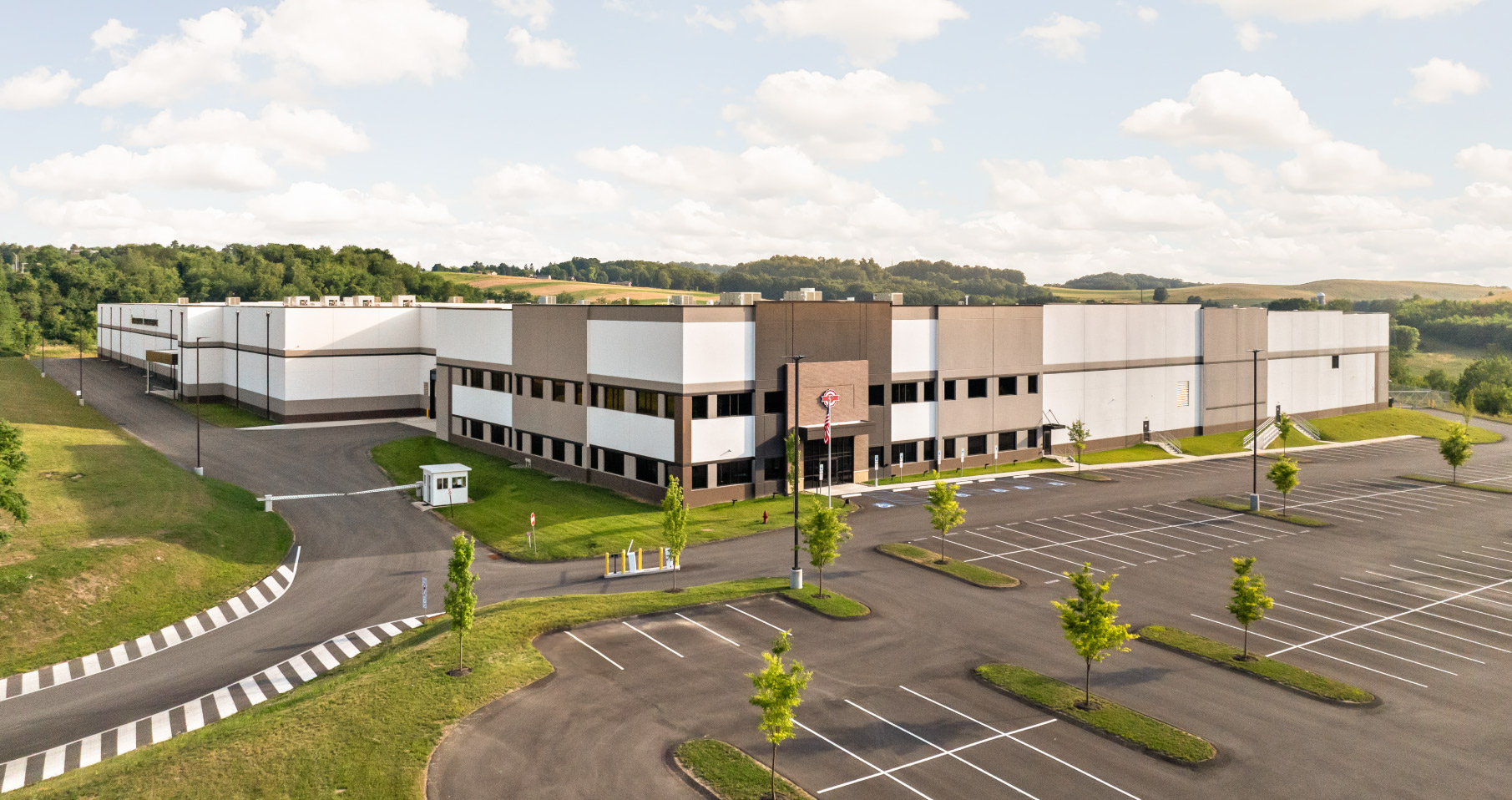 Large industrial building with parking lot and trees on a sunny day.