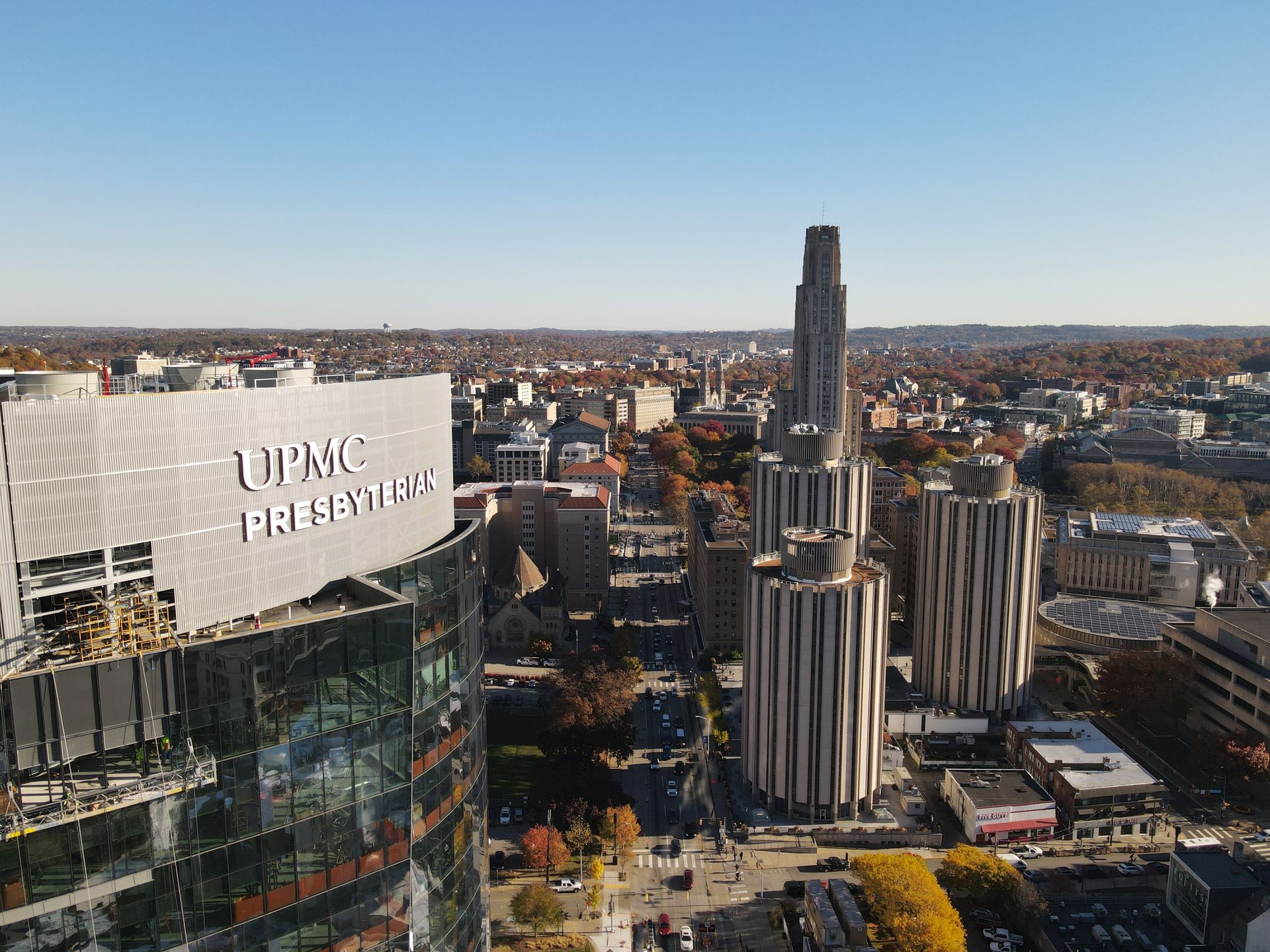 Aerial view of Pittsburgh, PA: UPMC Presbyterian building in foreground, Cathedral of Learning visible, clear sky.
