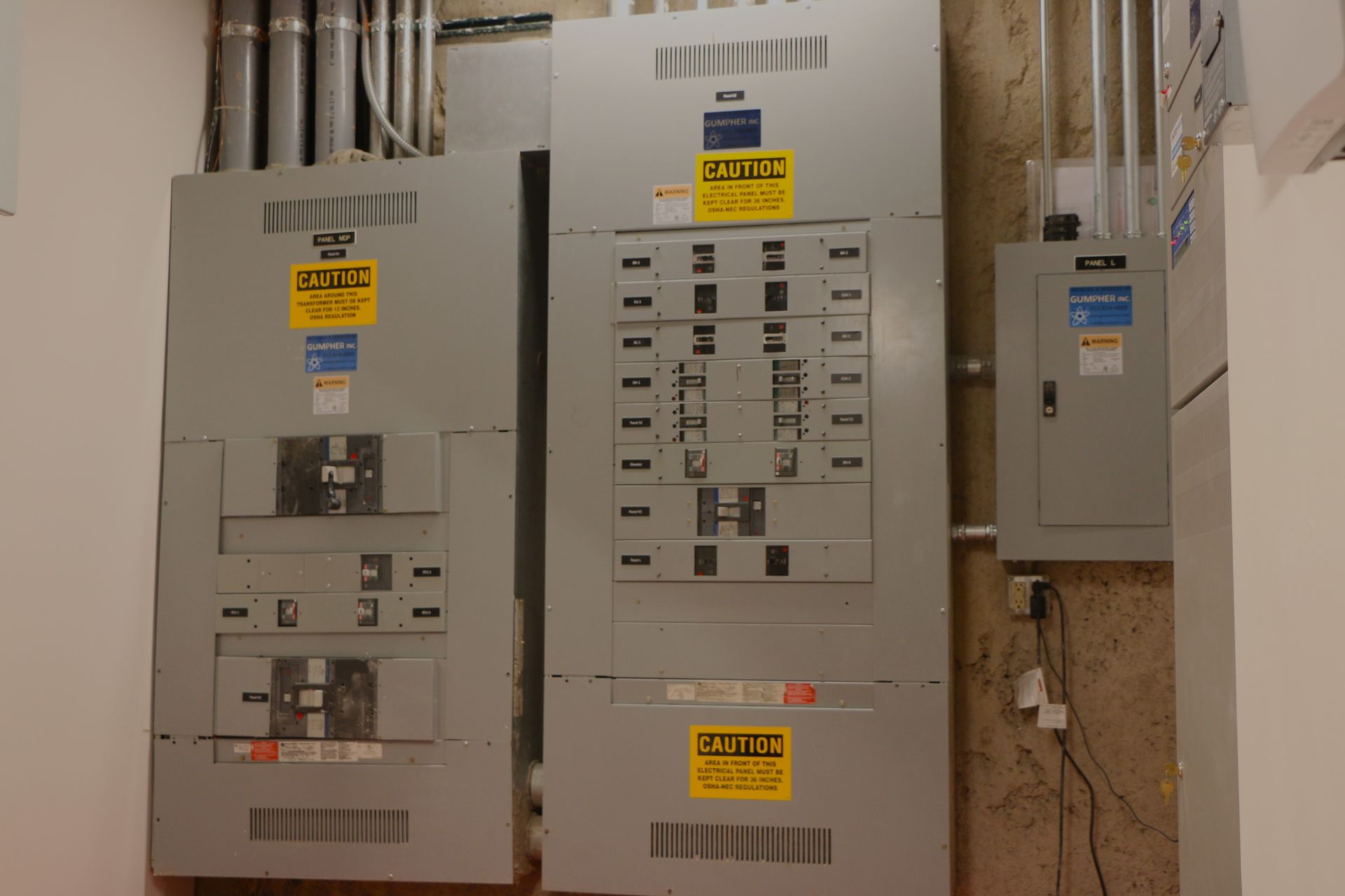 Electrical panels with conduits, yellow safety labels, in a utility room.