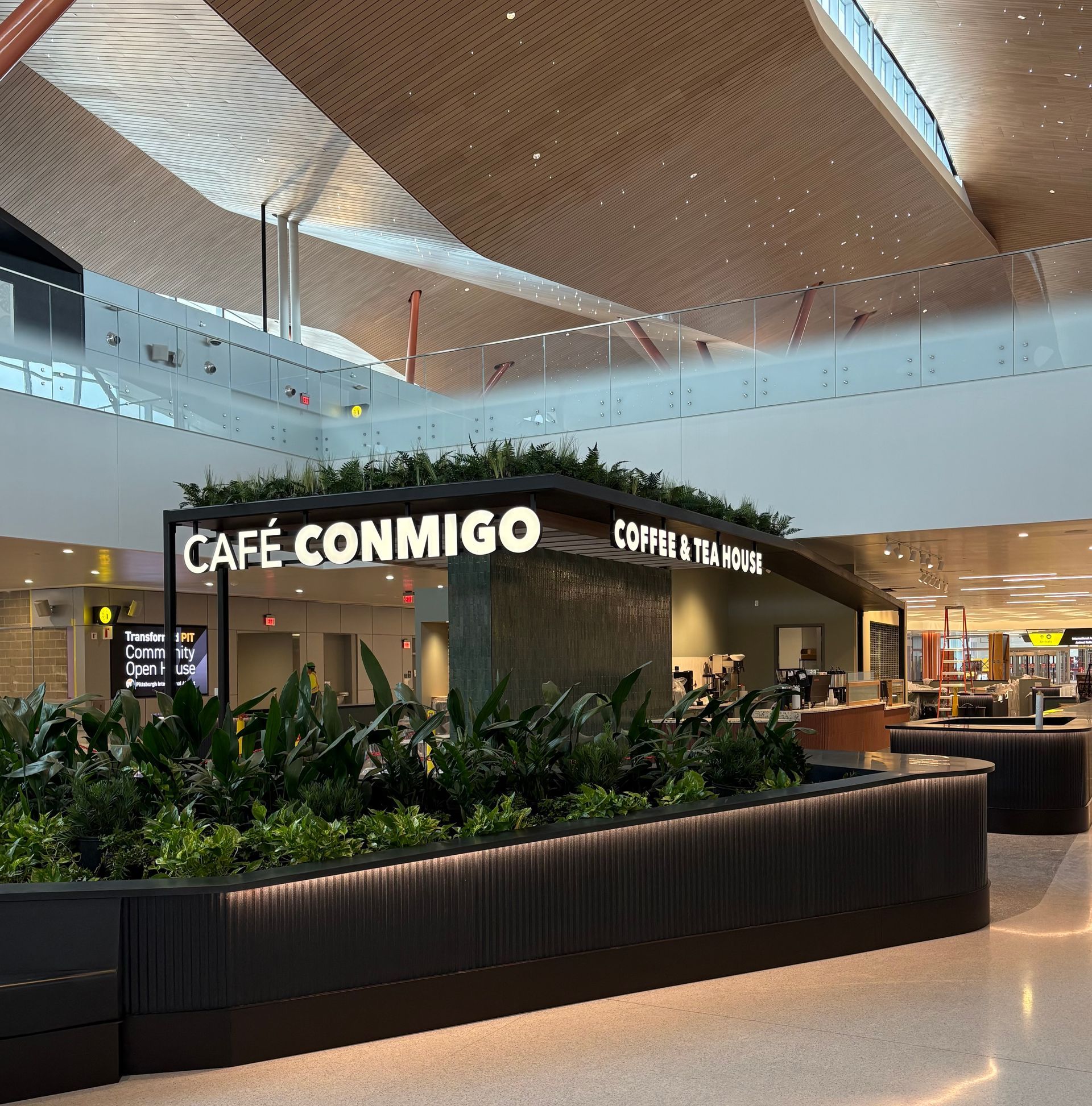 "Café Conmigo coffee shop in an airport with a black planter box and sign."