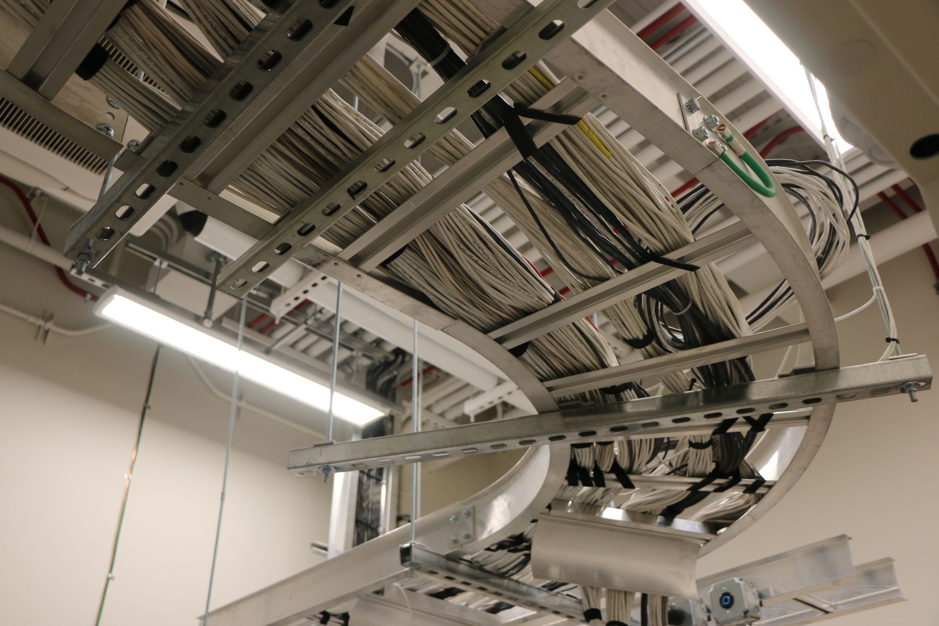 Overhead cable trays filled with bundles of wires, curving along the ceiling in an office setting.