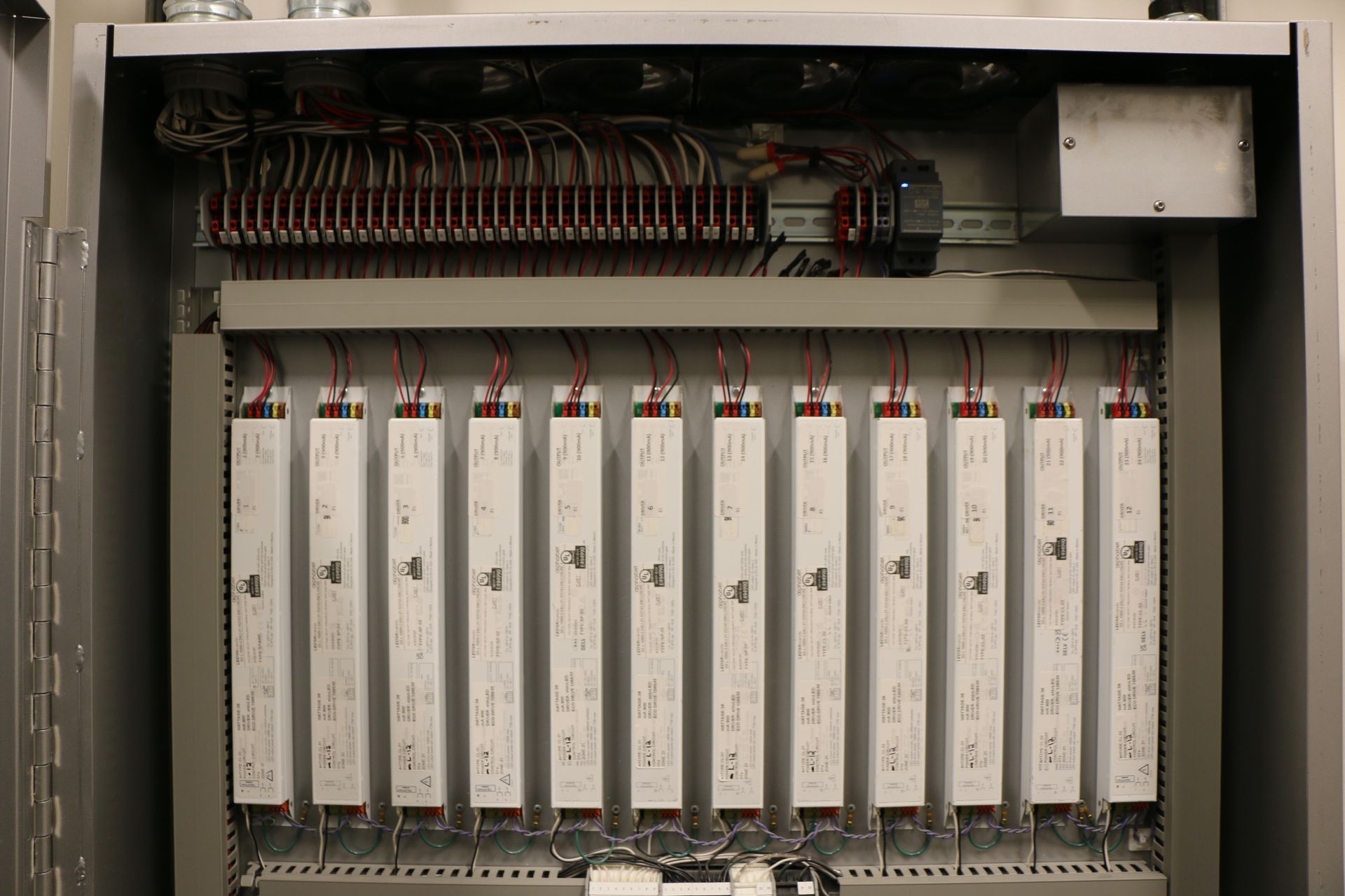 An open electrical control panel with rows of white rectangular devices and wiring.