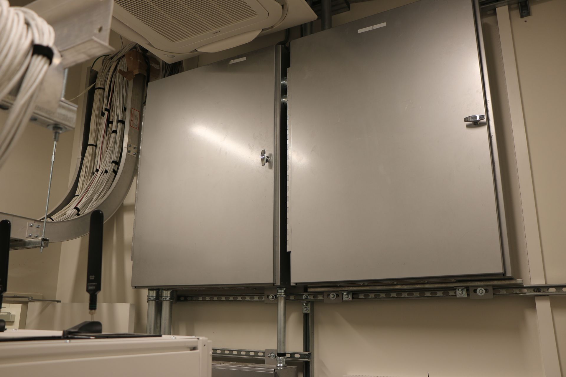 Two gray metal electrical panels mounted on a wall, with visible conduit and cables.