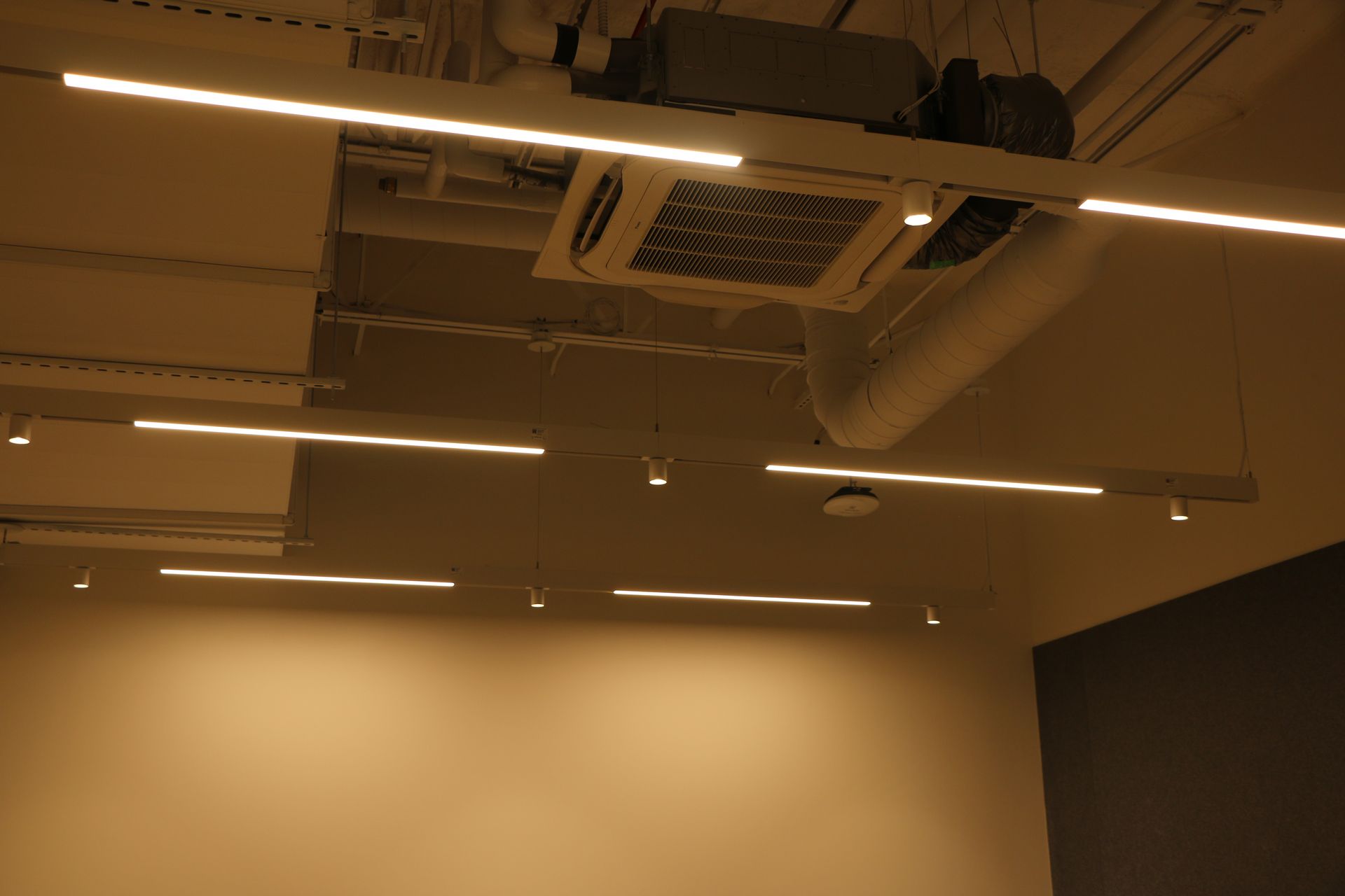 Modern office ceiling with linear lights, ductwork, and an air conditioning unit.