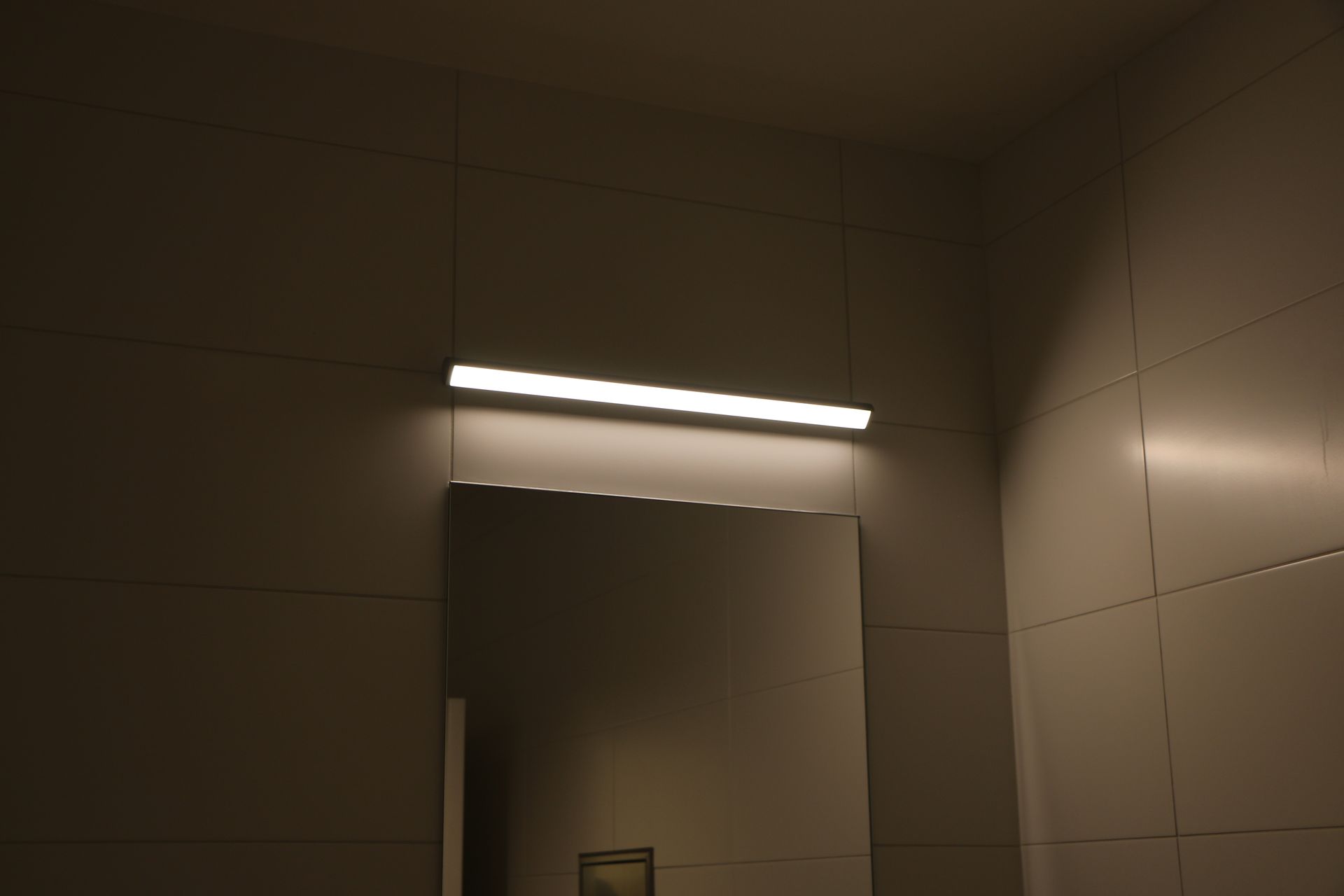 Lighted rectangular fixture above a mirror in a tiled room.