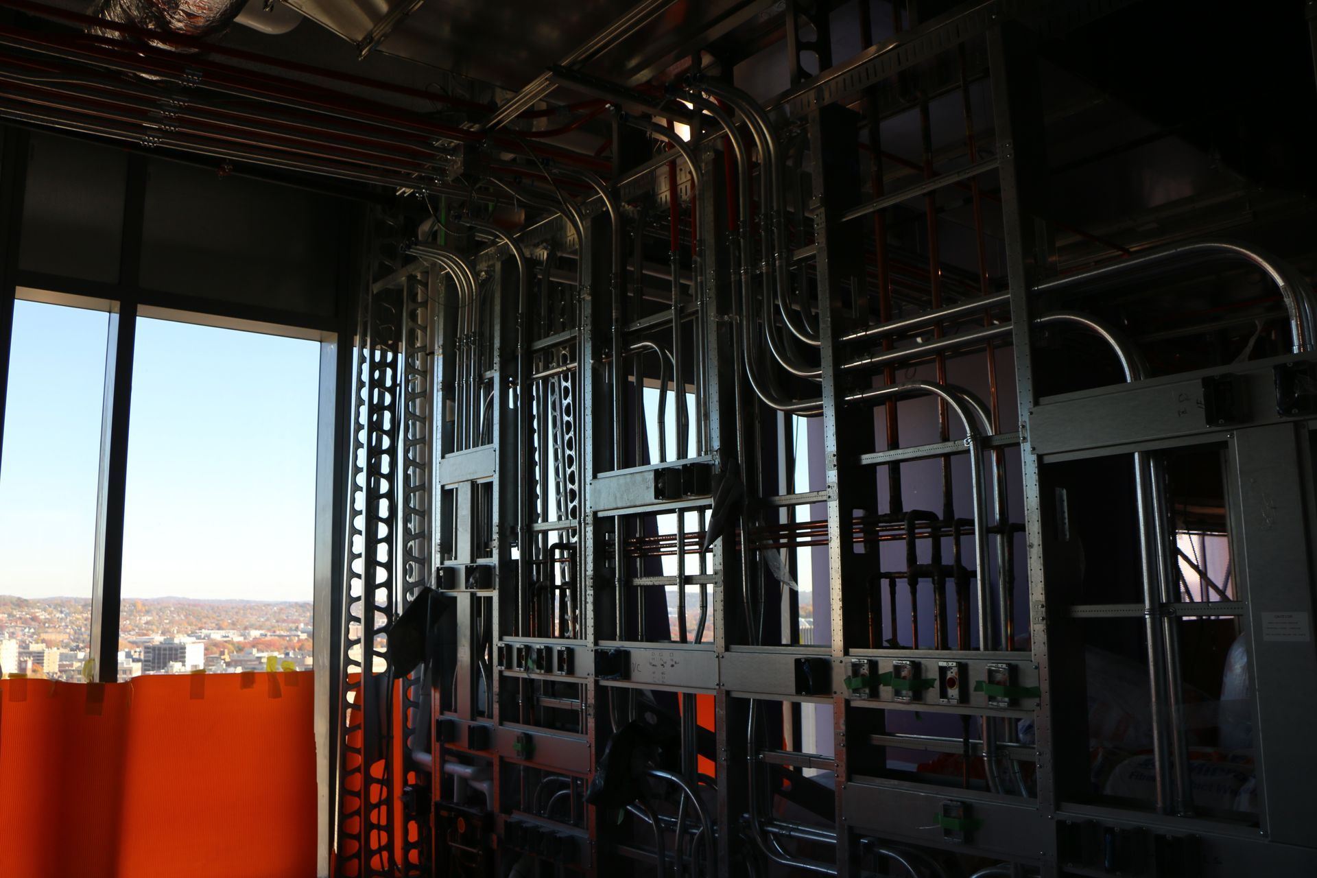 Metal conduit and electrical boxes inside unfinished building frame, orange safety barrier visible.