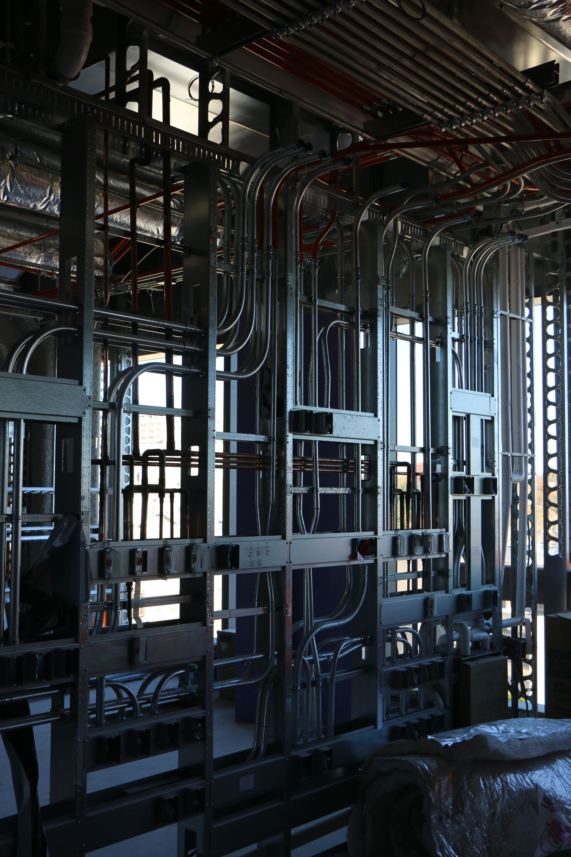 Steel framing and conduit pathways within a construction site's wall cavity; red wires.