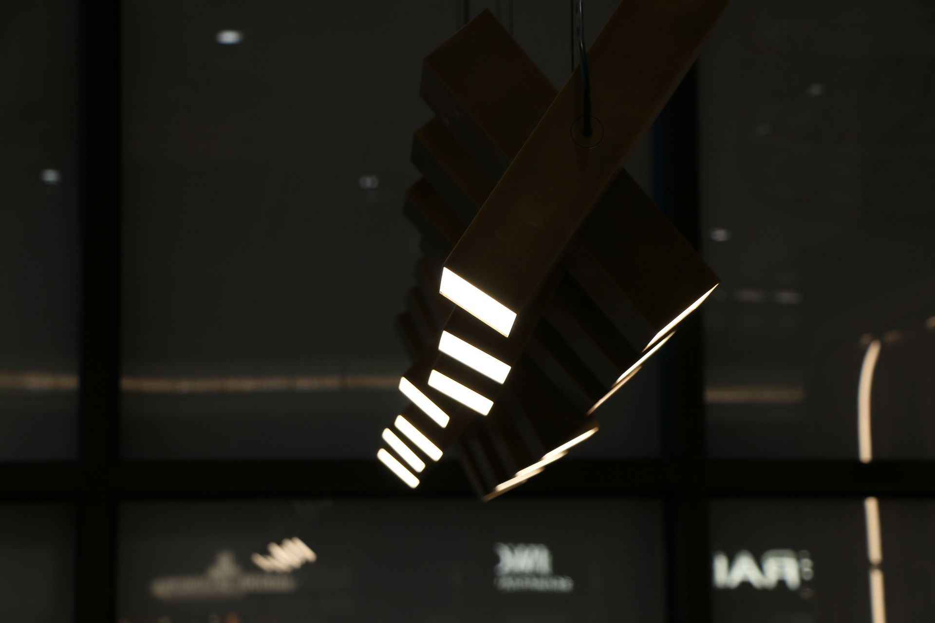 Hanging, geometric light fixture with several glowing rectangular openings against a dark background.