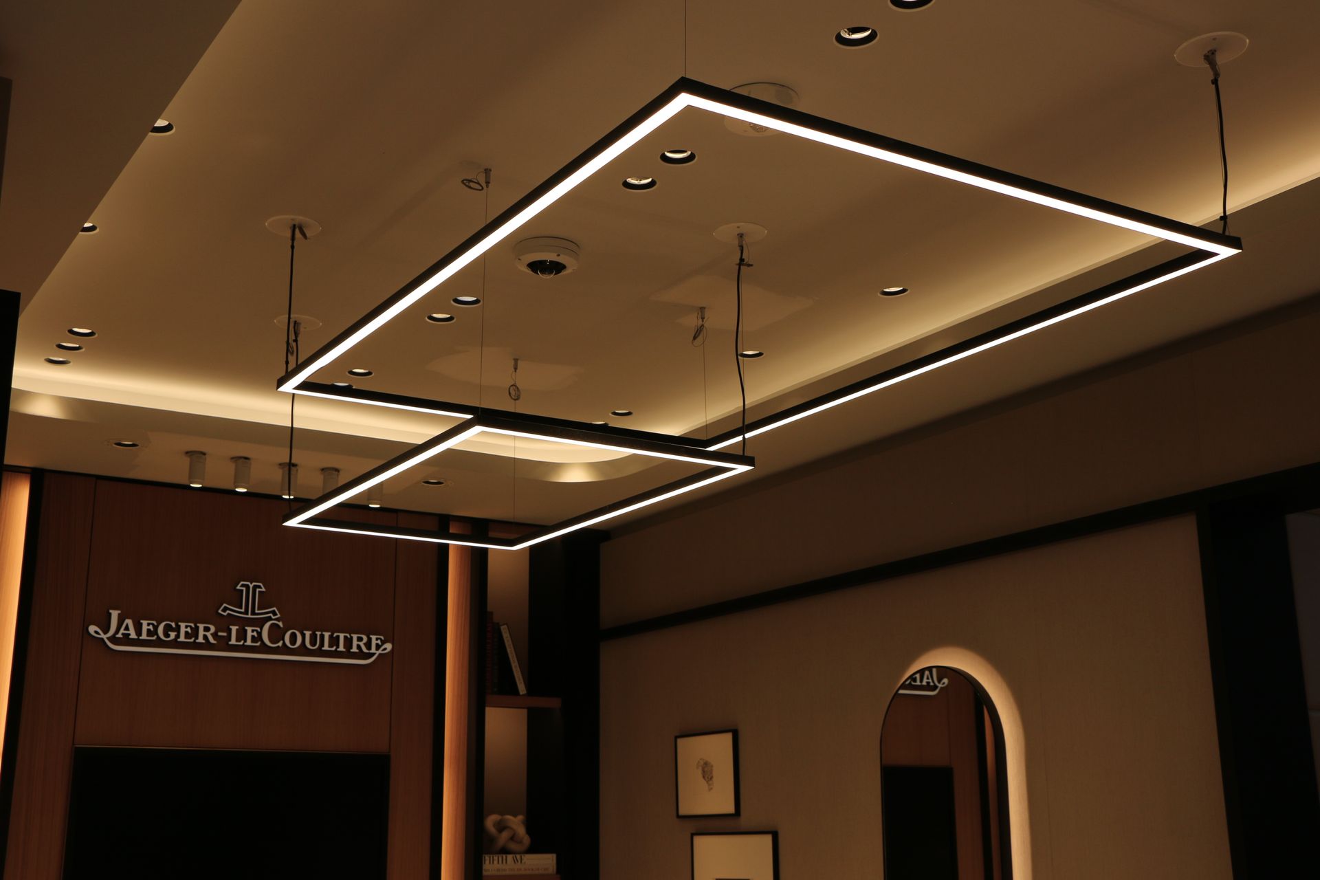 Two rectangular, modern pendant lights in a luxury watch store, next to the Jaeger-LeCoultre sign.