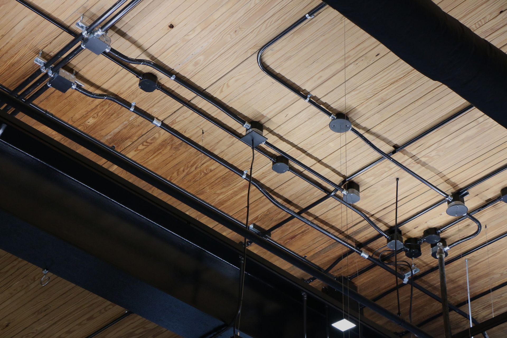 Exposed electrical conduit and junction boxes run across a wooden ceiling.