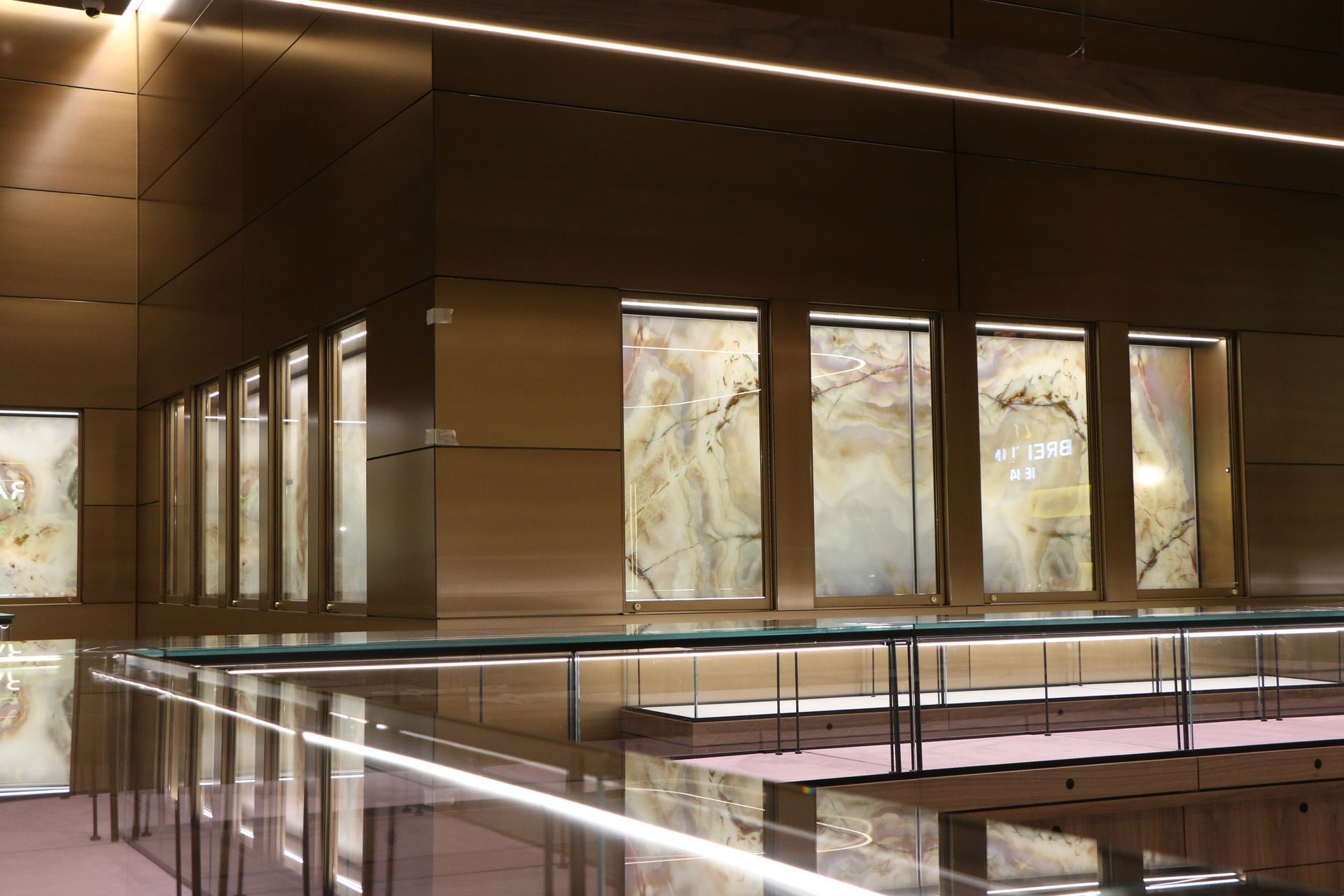 Displays of illuminated stone slabs in a modern, gold-toned architectural space with glass railing.