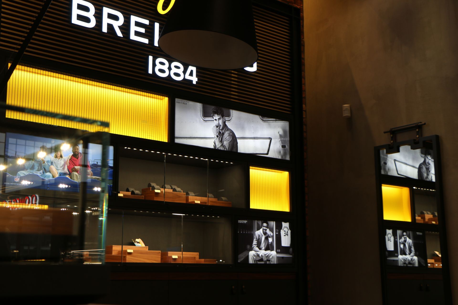 Breitling watch display with illuminated cases. Logo and vintage photos visible. Dark setting with yellow accents.