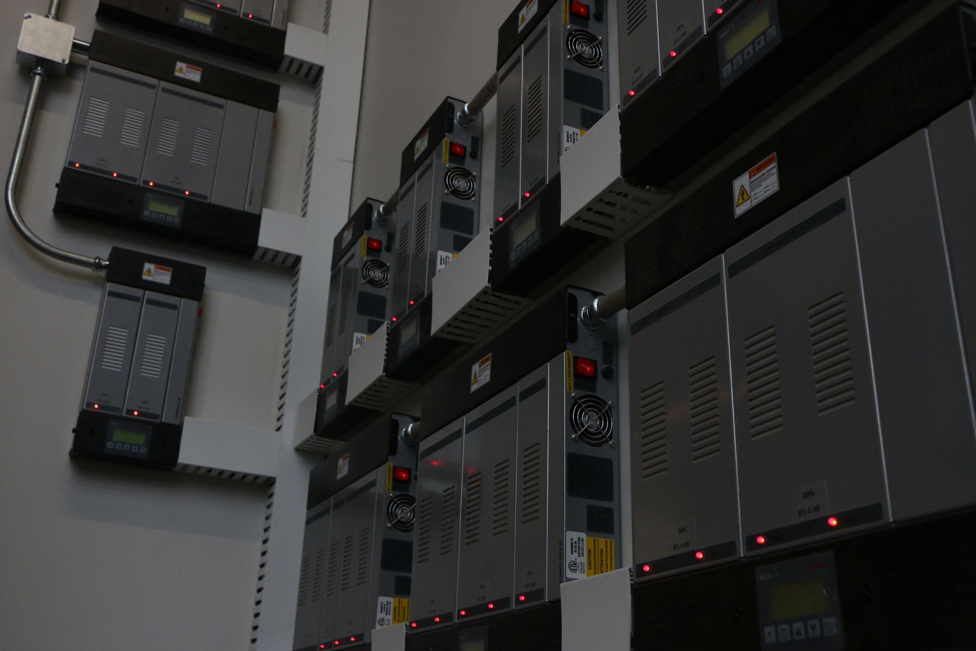 Wall of industrial electrical equipment with meters and red lights.