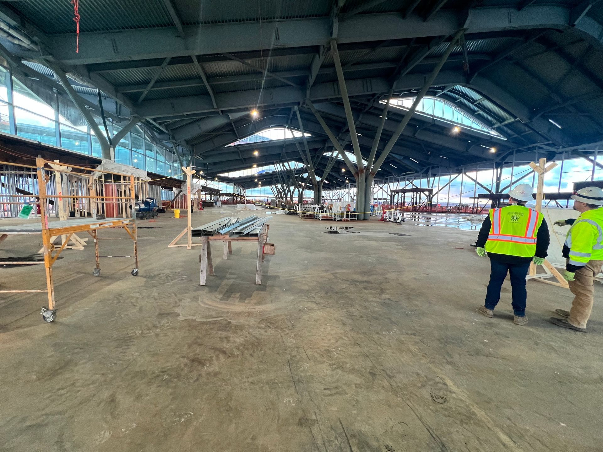 Two construction workers in safety vests and hard hats surveying a building site at dusk.