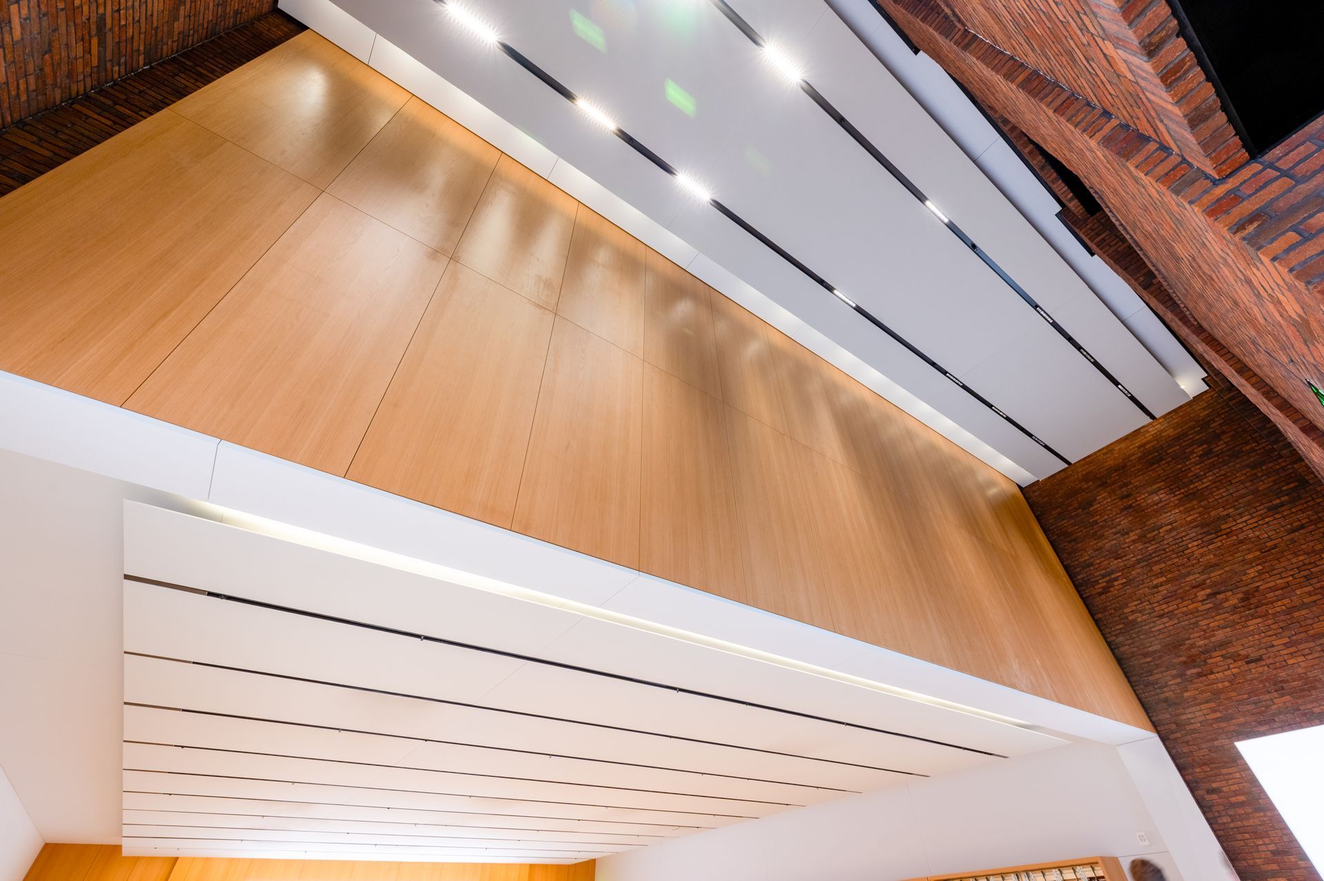Interior view of wooden paneling and a white ceiling with recessed lighting; brick wall on the right.