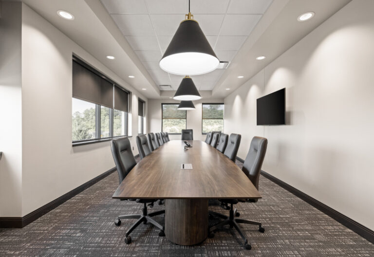 Conference room with long wooden table, black chairs, and pendant lights.
