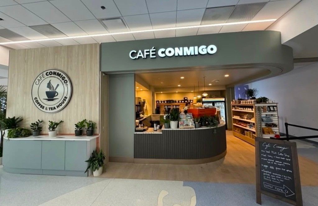Exterior of Café Conmigo coffee shop with sign, plants, and an open entrance.