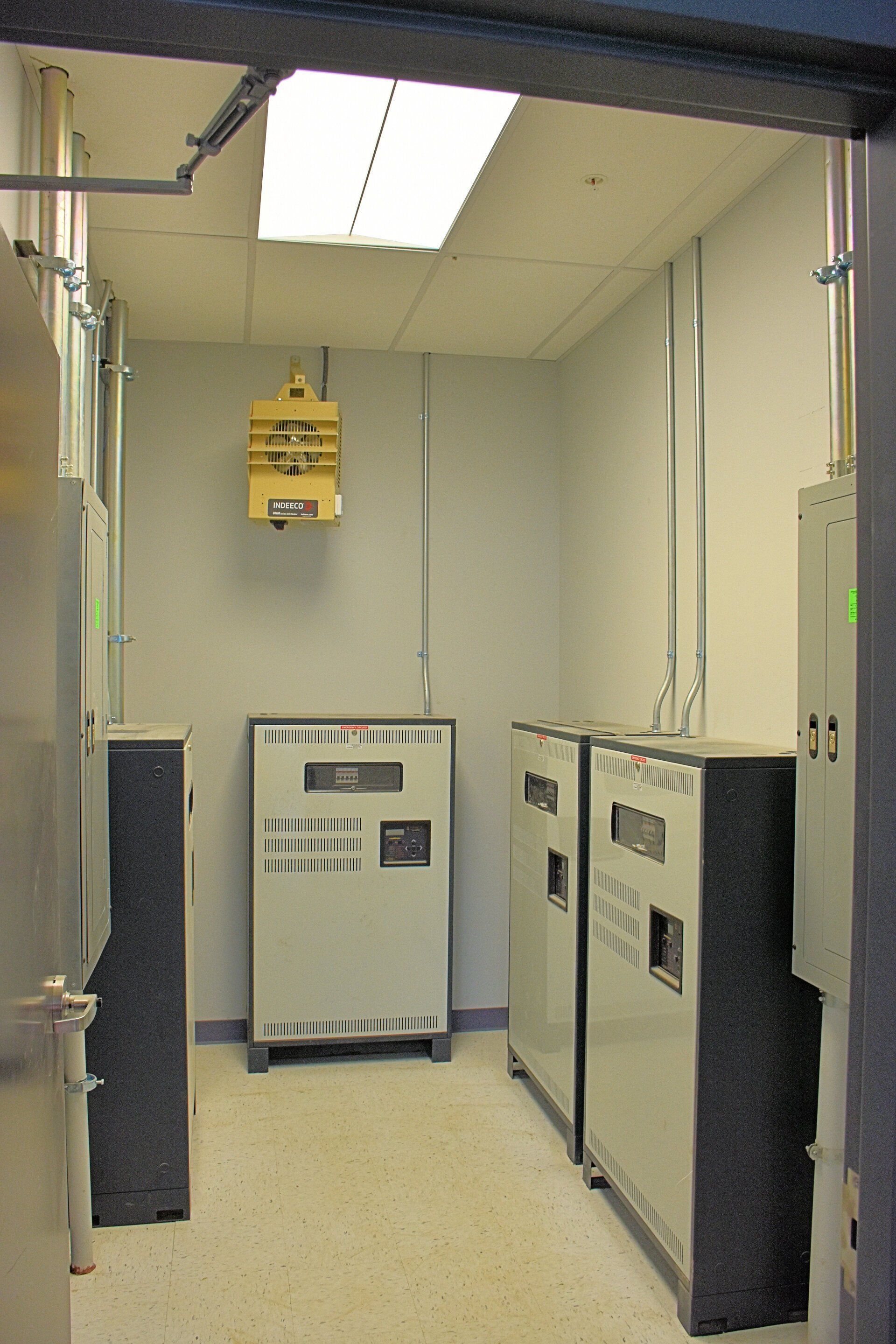 Small electrical equipment room with gray machinery and a fluorescent ceiling light.