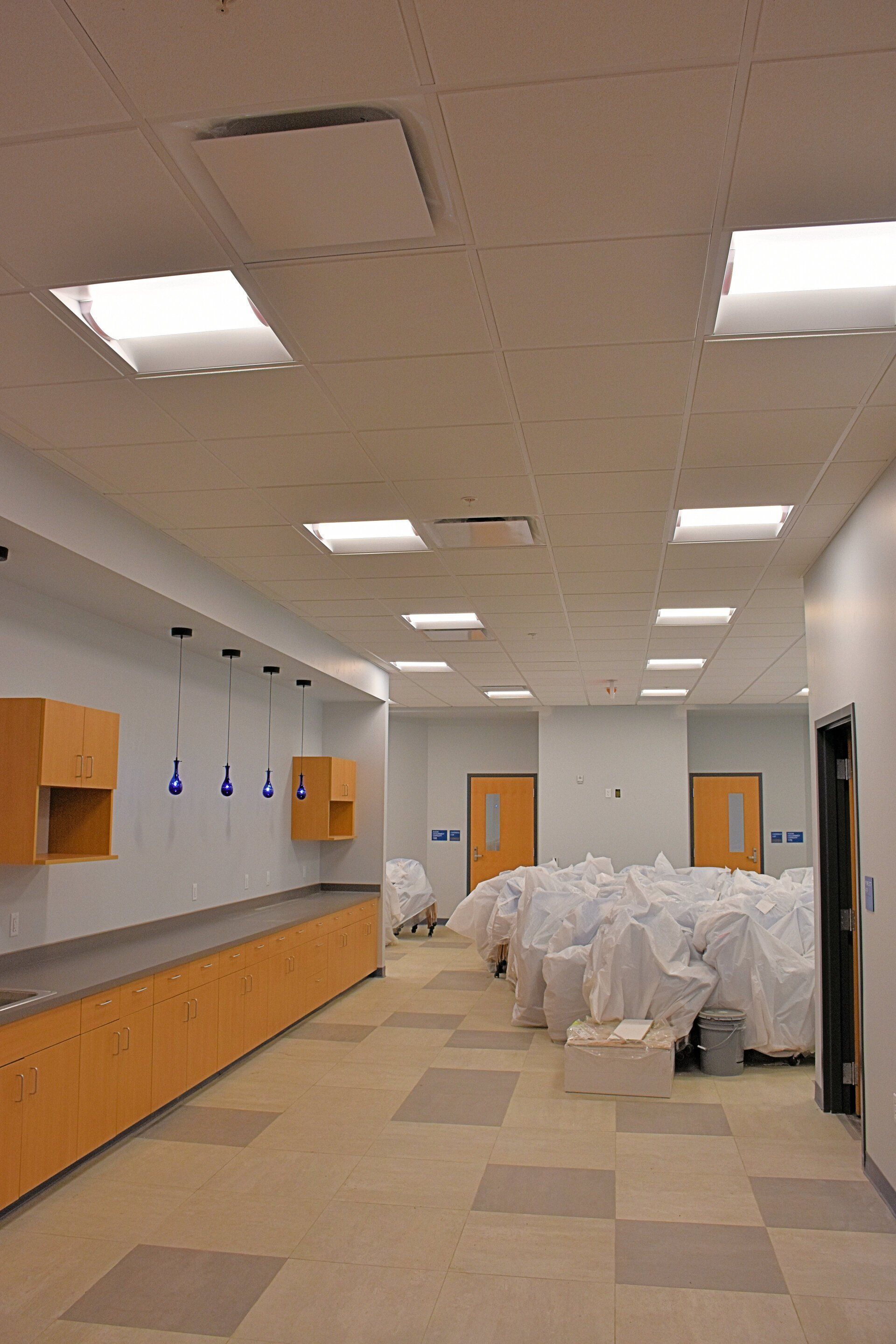 Empty hallway with tan cabinets, square ceiling lights, and doors. White bags cover the floor.