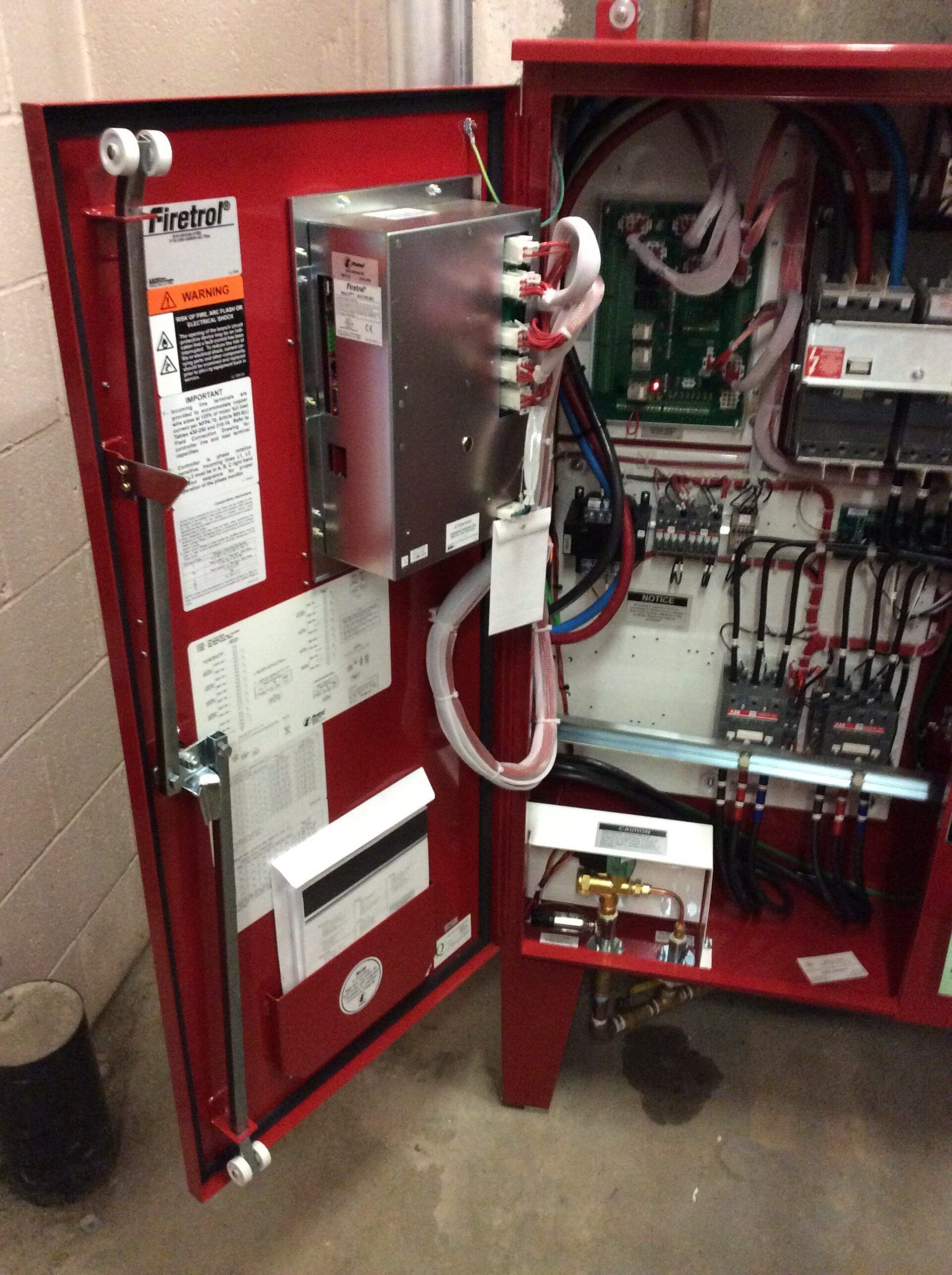 Red fire alarm control panel cabinet with open door, electronic components visible.