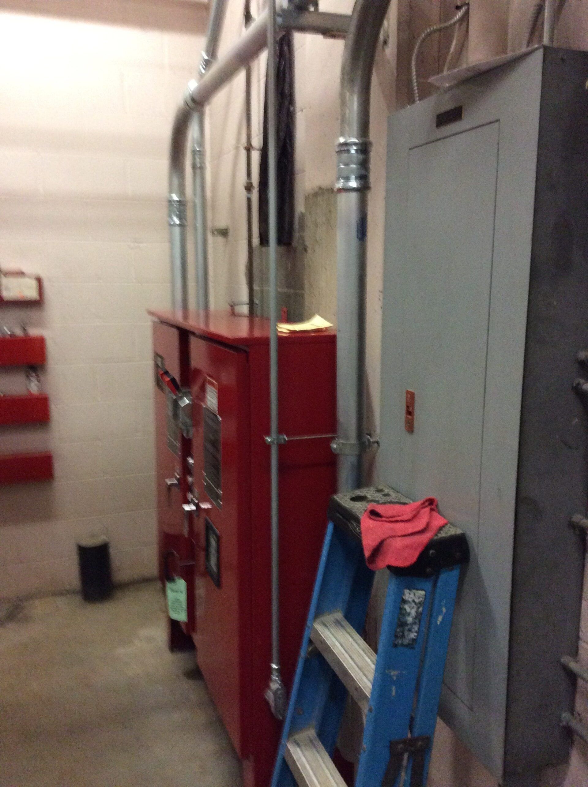 Electrical equipment room with red and gray panels, conduit, and a blue ladder with a red cloth.