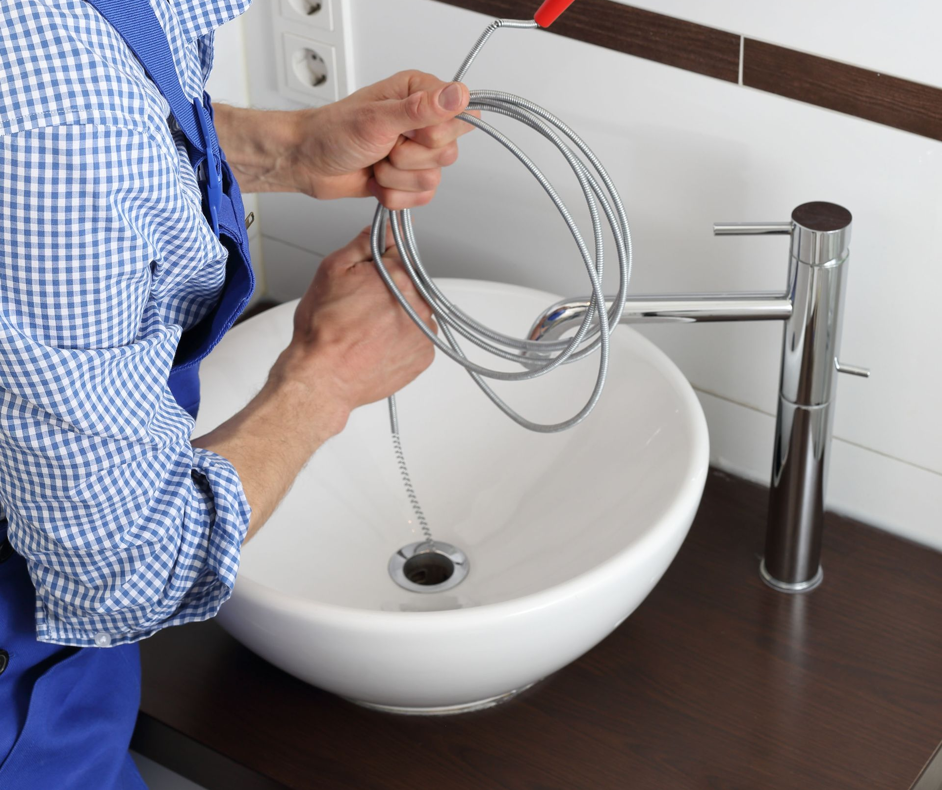 Plumber using a snake tool to unclog a bathroom sink in a modern bathroom.