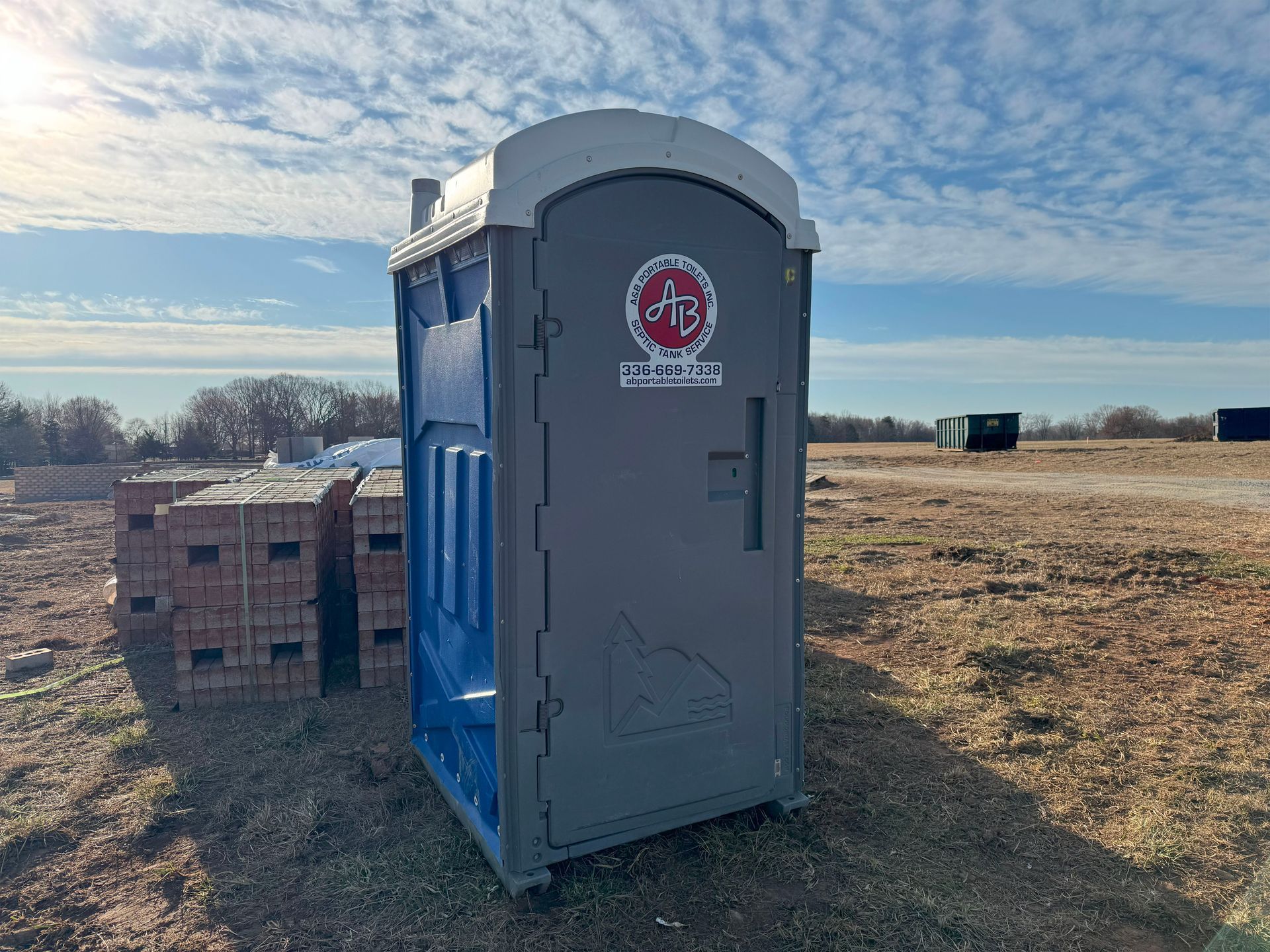 A portable toilet is sitting in the middle of a field.