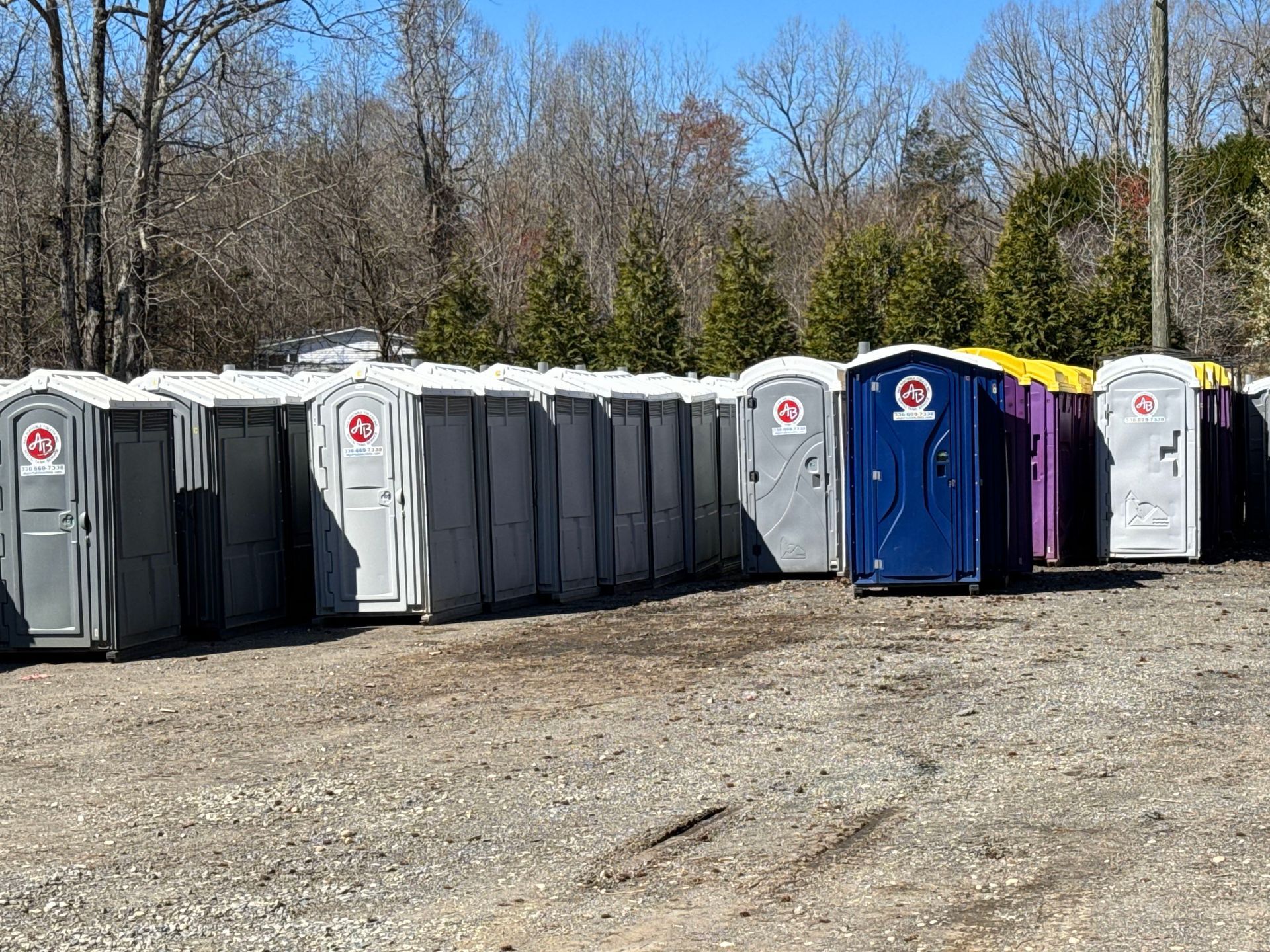 A row of portable toilets are lined up in a dirt field.