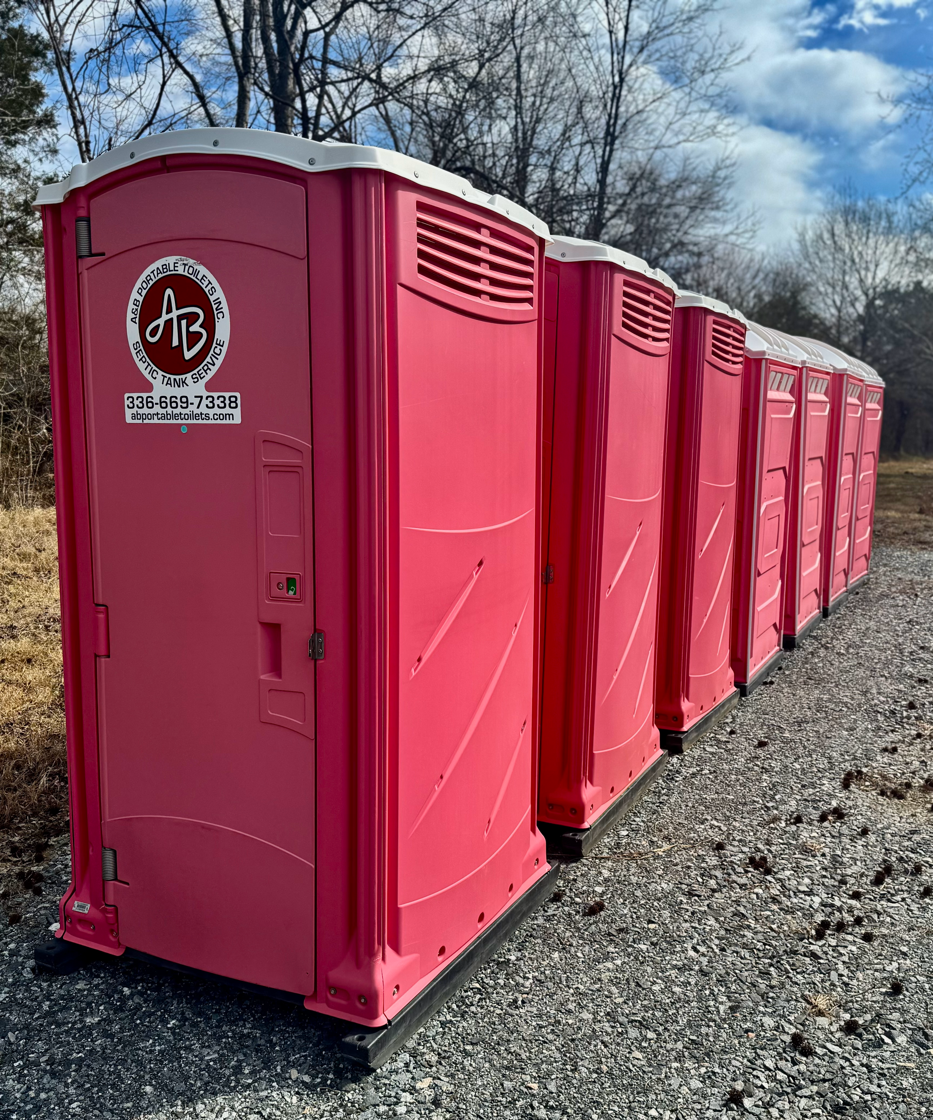 A row of pink portable toilets are lined up in a gravel lot.