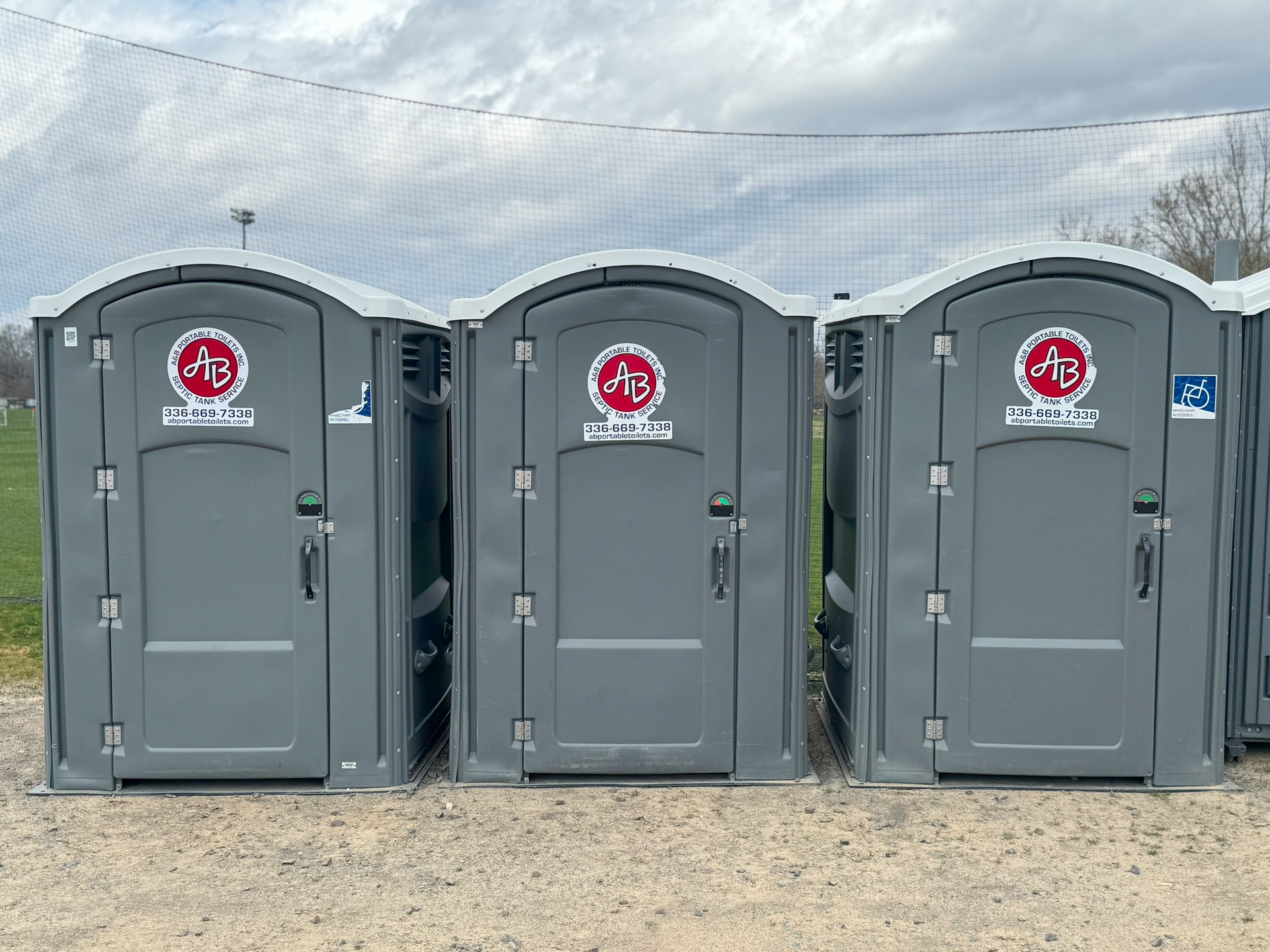 Three portable toilets are lined up in a row on a dirt field.