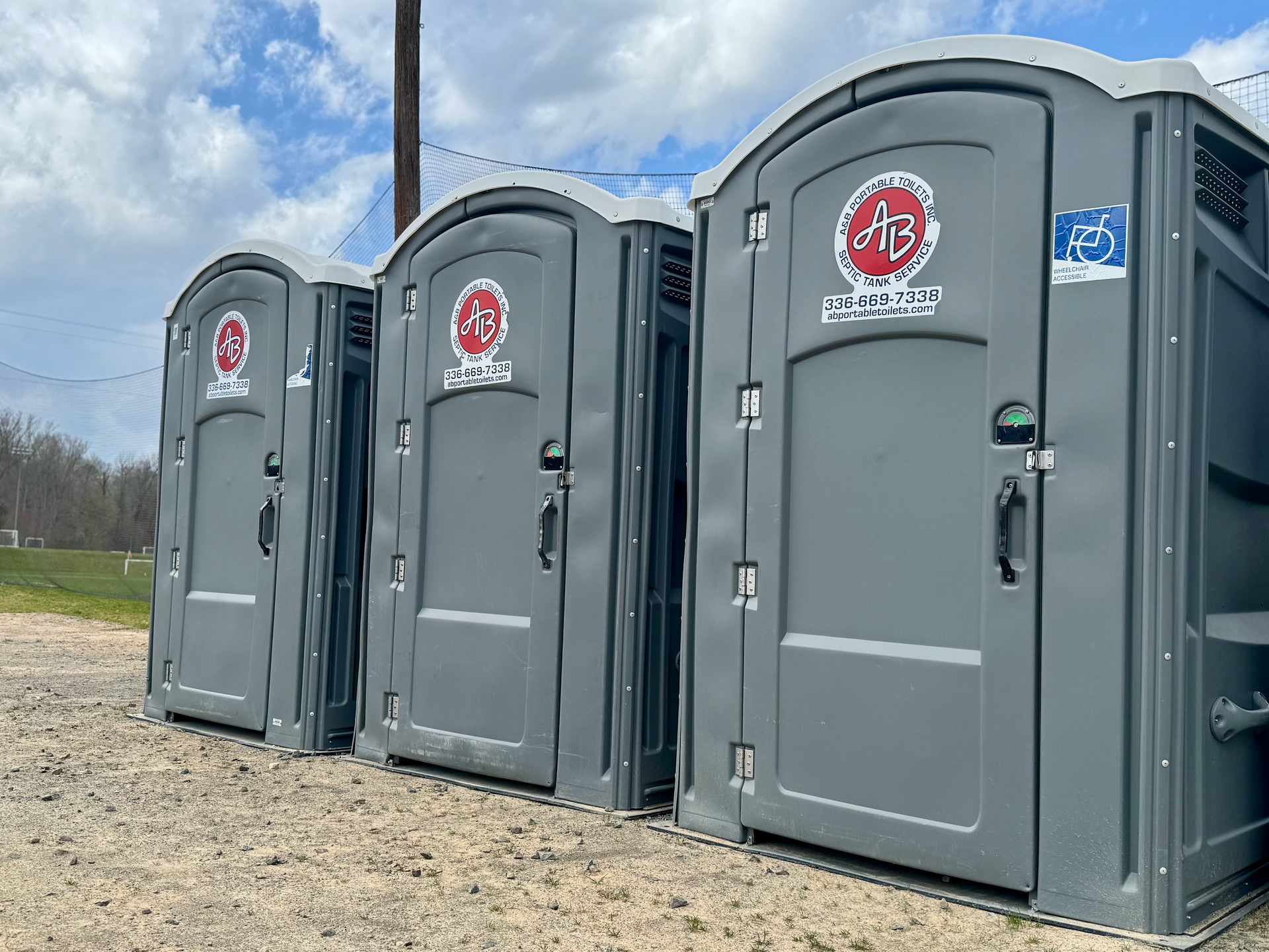 A row of portable toilets are lined up in a dirt field.