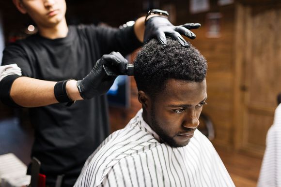 Man getting haircut at salon; barber using comb. Brick wall, wooden ceiling.