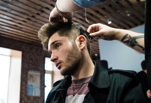 Man getting haircut at salon; barber using comb. Brick wall, wooden ceiling.