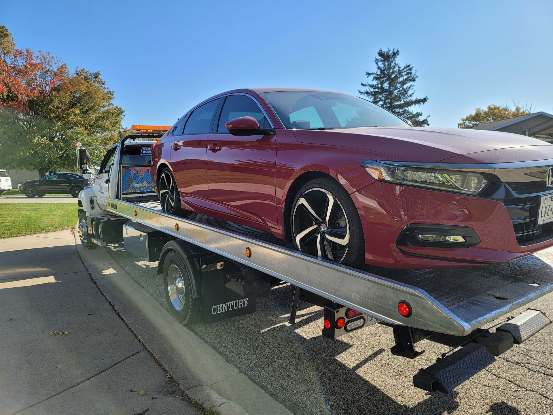 Red Honda Accord sedan on a tow truck, parked on a street on a sunny day.