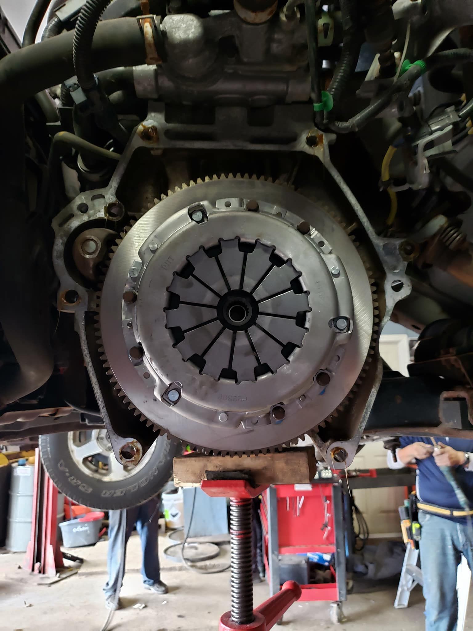 Car engine with a new clutch installed, being worked on in a garage.