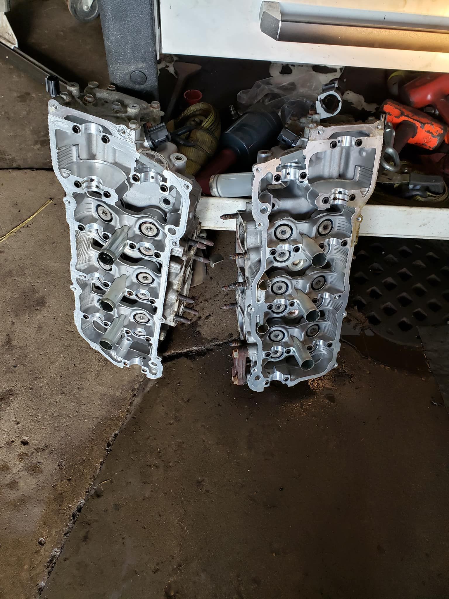 Two silver engine cylinder heads resting on a dirty surface.