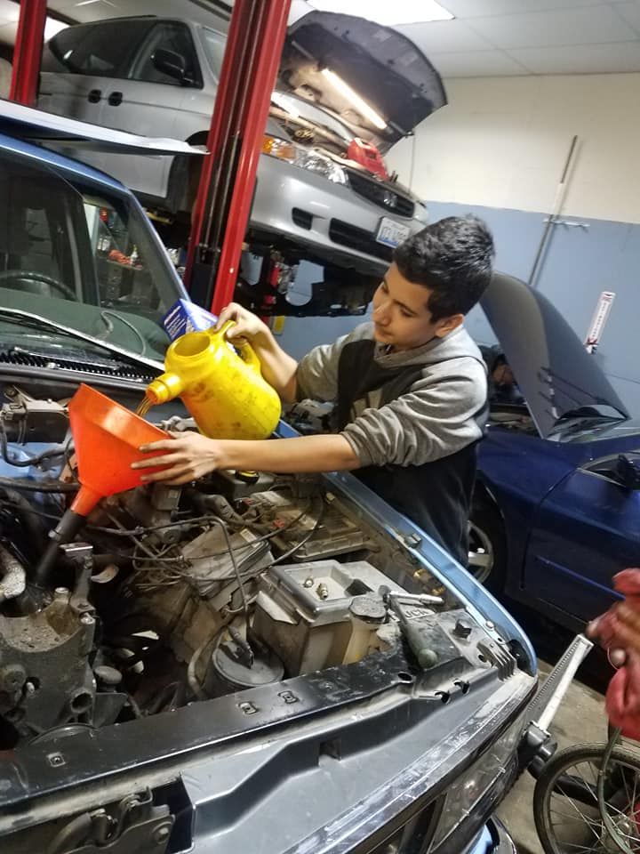 Person pouring oil into a car engine at an auto repair shop.