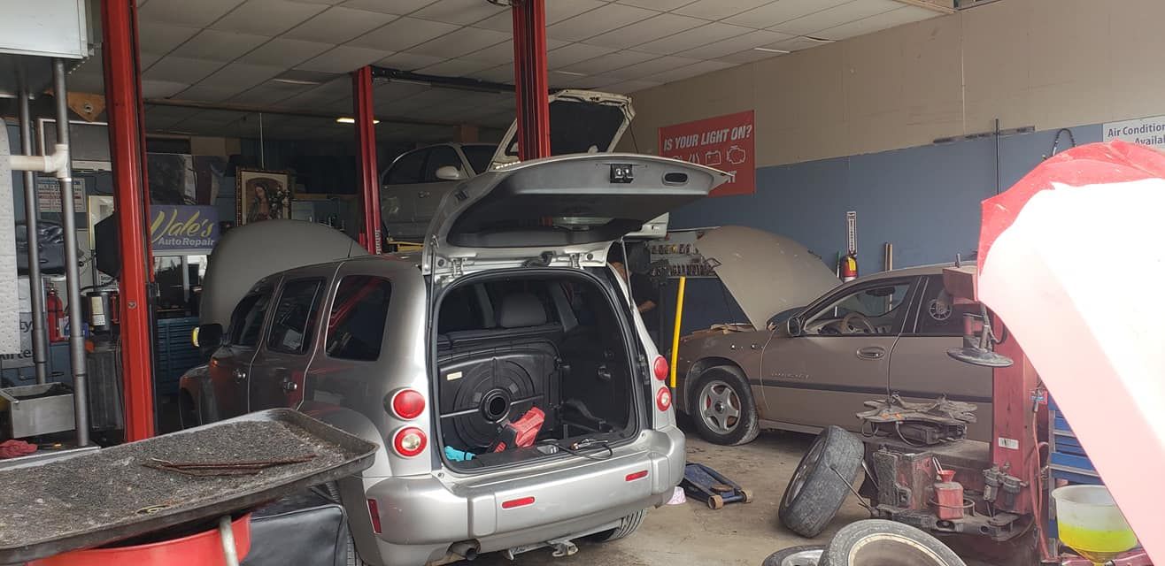 Inside a mechanic shop, a silver SUV has its rear open, and other cars are being worked on.