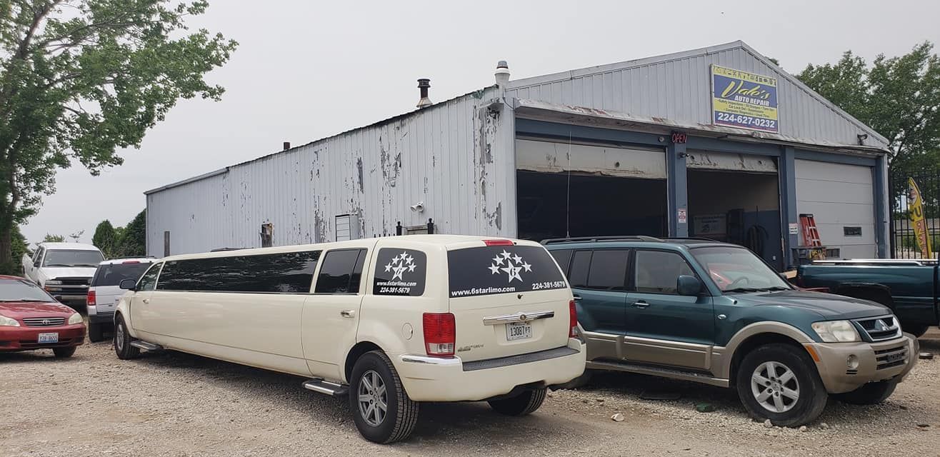 A white limousine parked outside a weathered building with a blue sign. Other vehicles are also parked nearby.