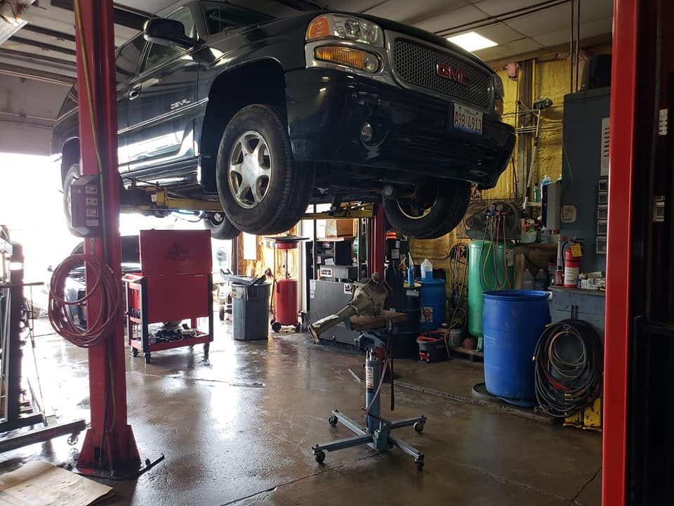 Black GMC Yukon SUV raised on a lift in a garage. Shop tools and equipment are visible.