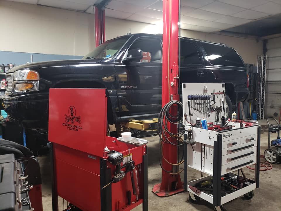 Black truck raised on a lift in a garage, tools and a red toolbox in the foreground.