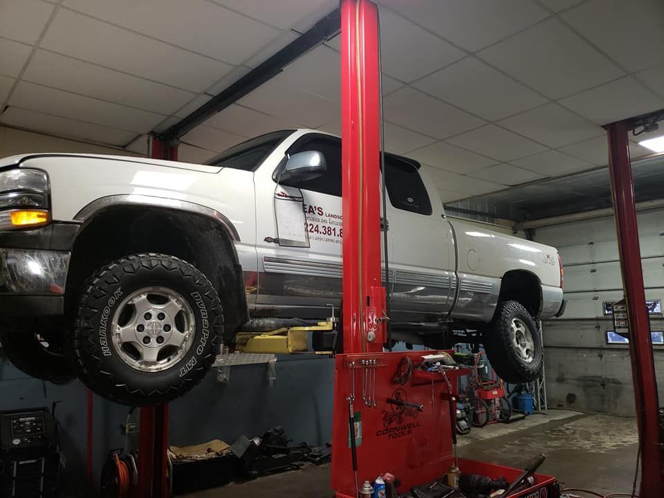 White pickup truck elevated on a red car lift inside a garage.